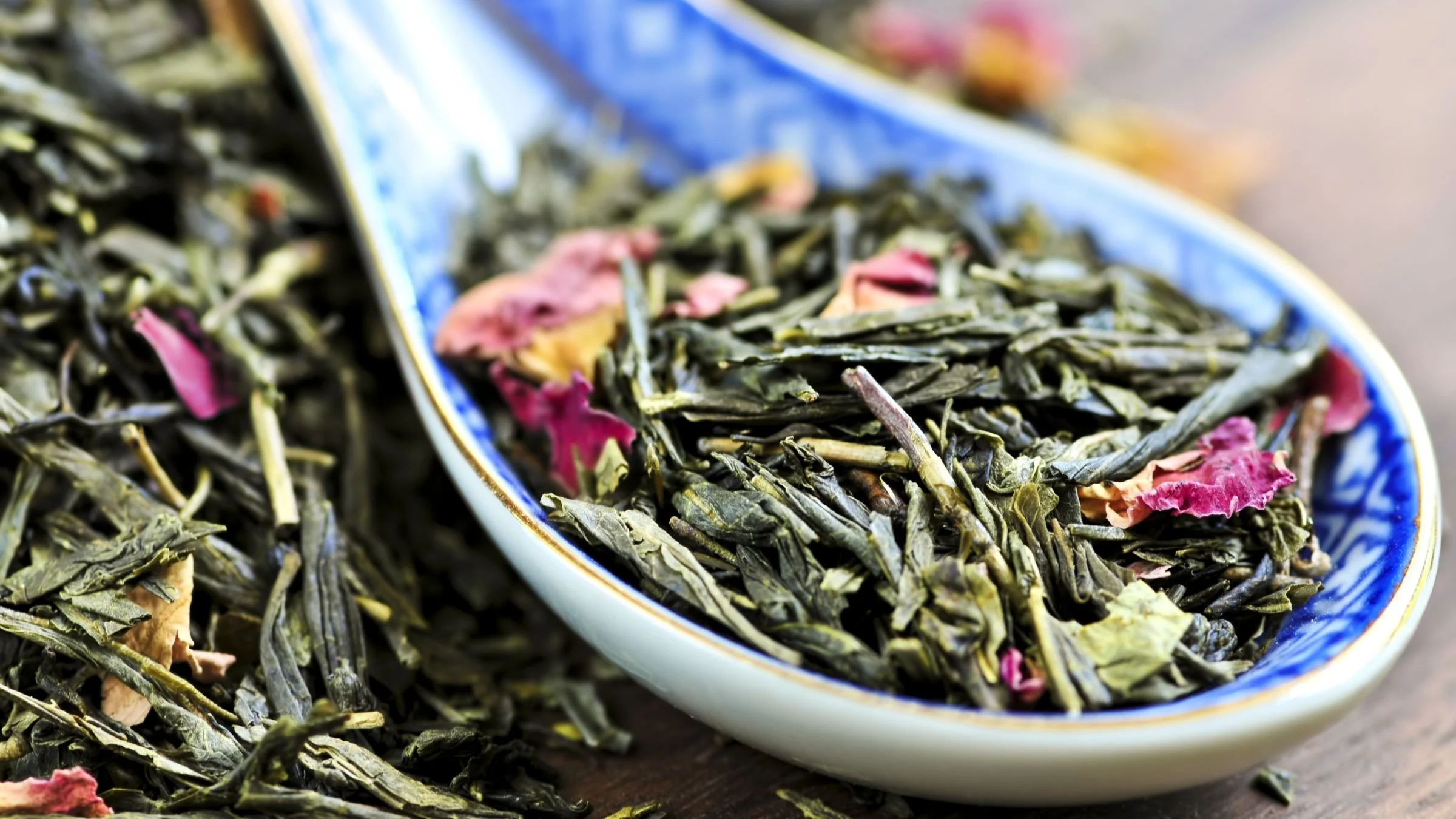 Close-up of dried green tea leaves with pink flower petals in a blue and white ceramic dish.