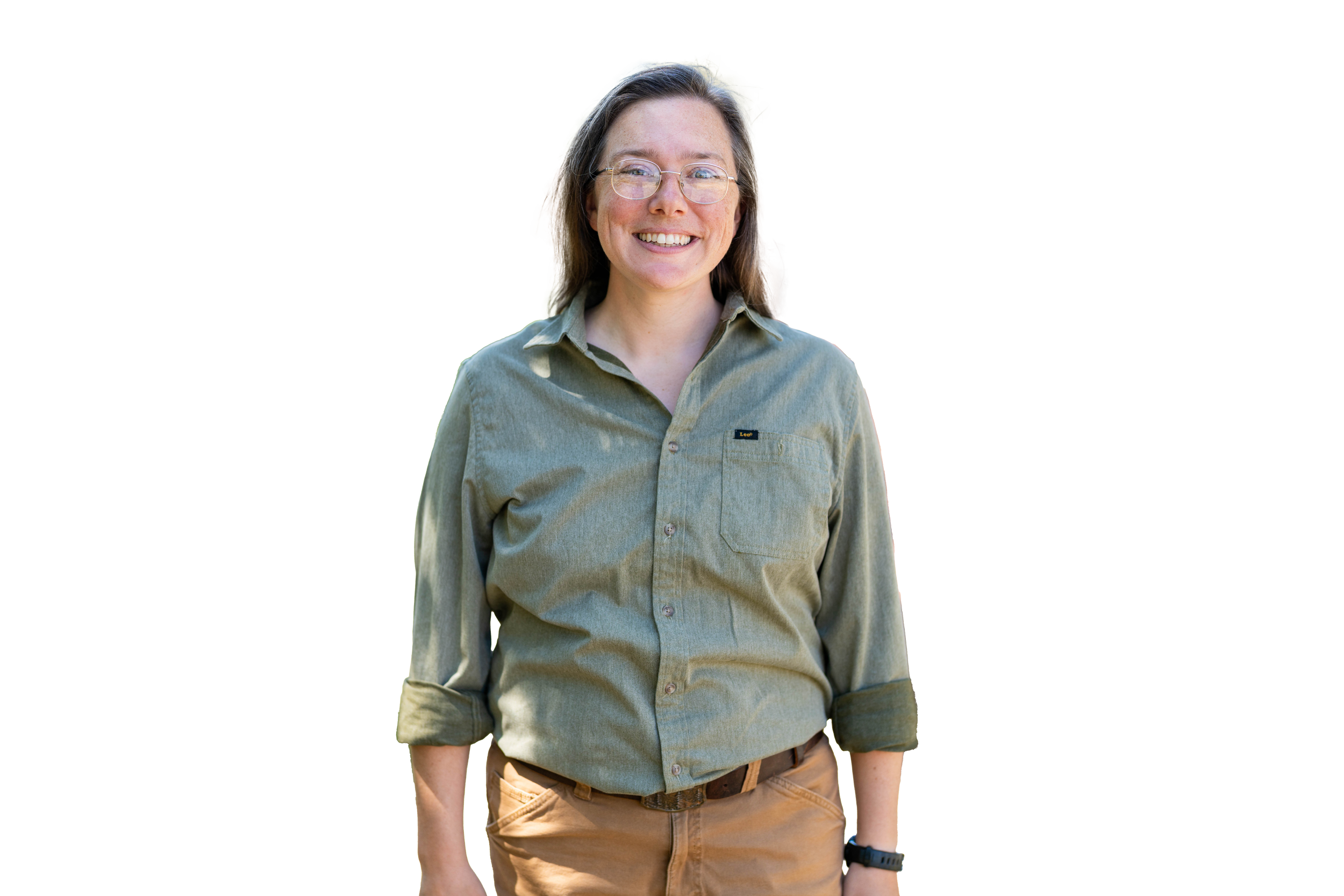 A smiling woman with glasses, wearing a green button-up shirt and khaki pants, standing outdoors.