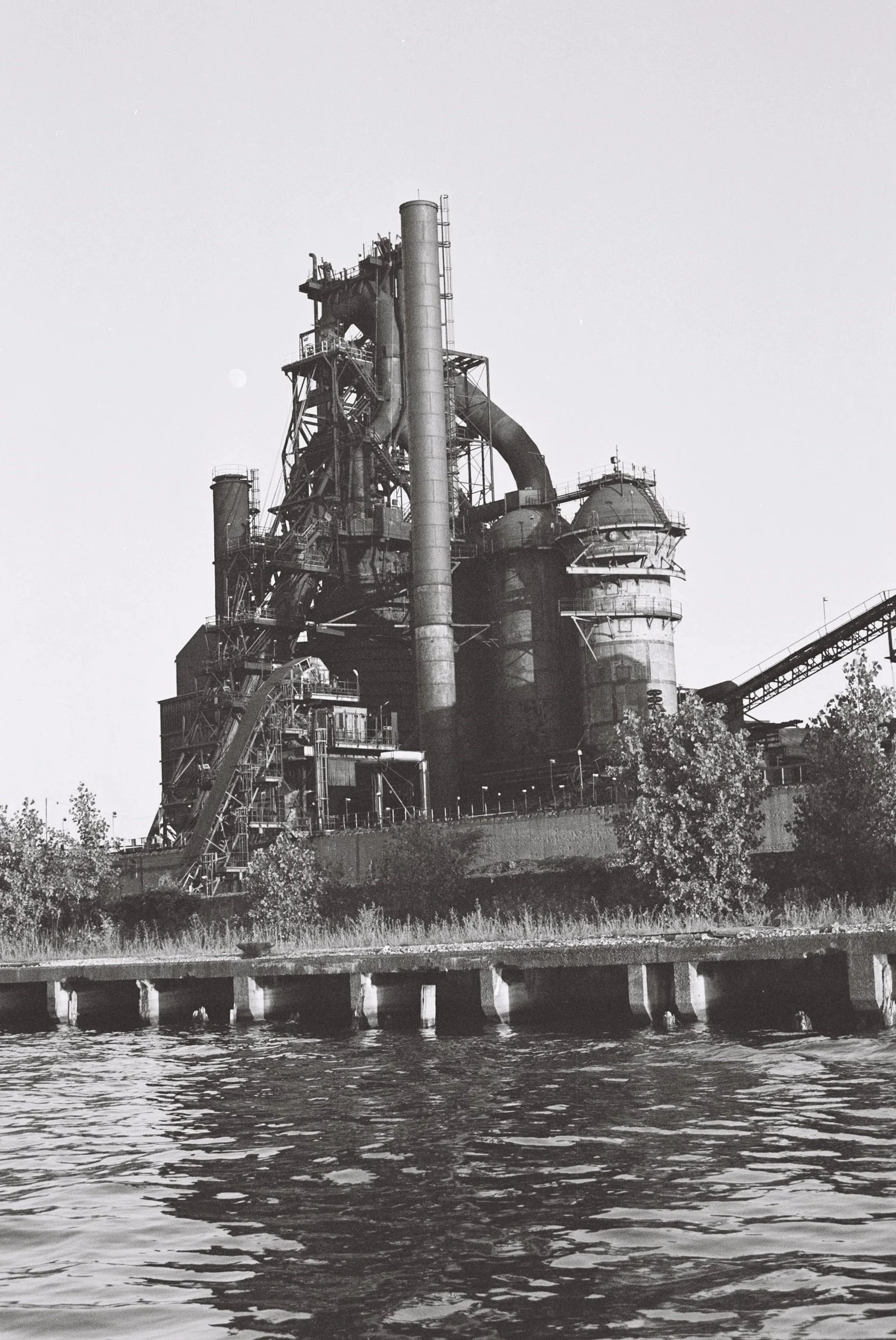 Black and white photo of an industrial factory with large smokestacks next to a body of water.