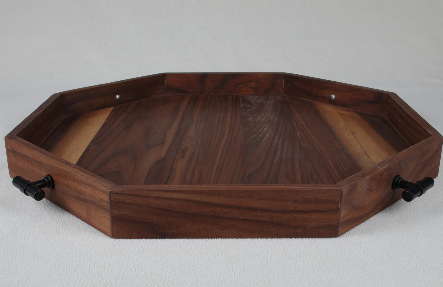 A wooden tray with a hexagonal shape and black handles on two sides, placed on a white textured surface.