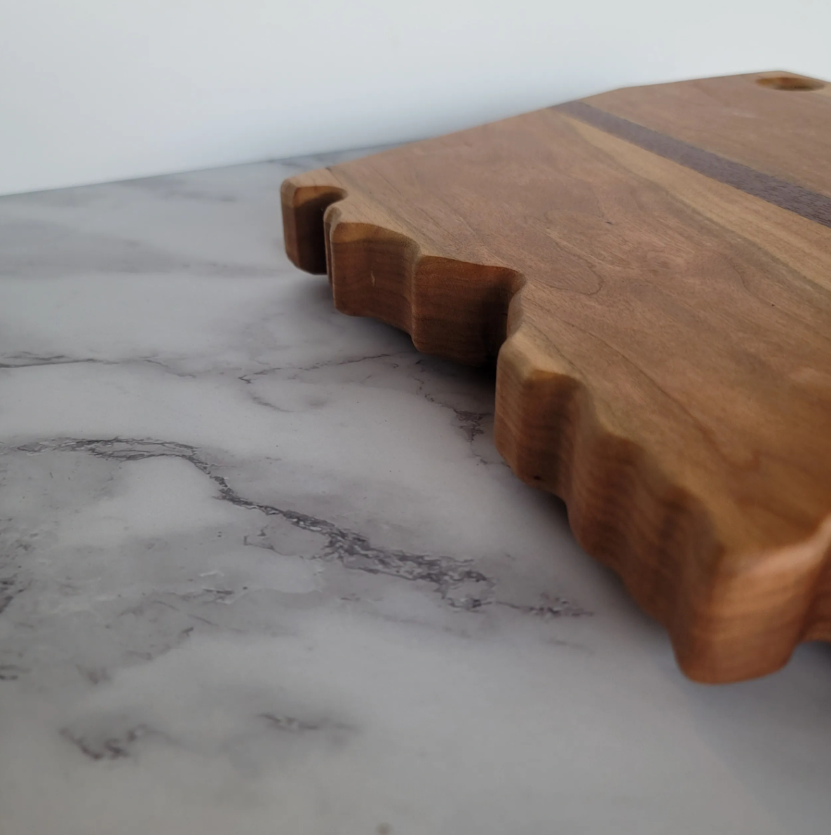 Close-up of a wooden cutting board on a marble countertop, showing the textured edge and wood grain.