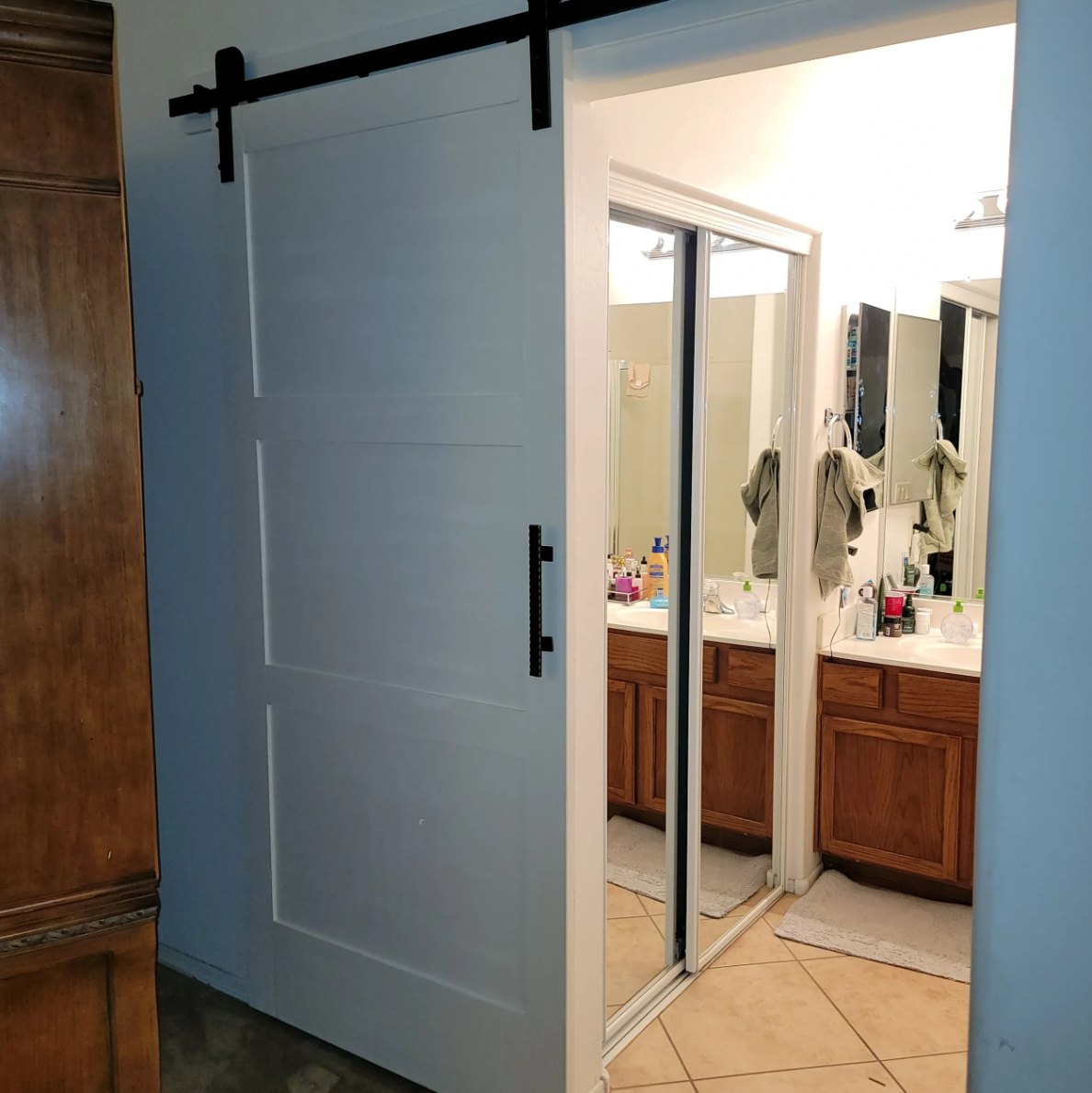 Bathroom with wooden cabinets and a mirror, shower area with sliding glass doors, towels hanging on hooks, and various toiletries on the counters.