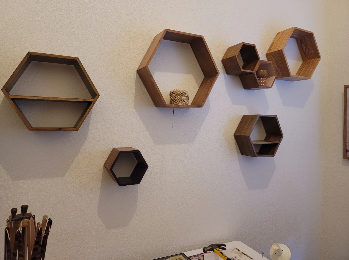 Wall decorated with various wooden hexagonal shelves, some containing small objects, with tools on a table below.