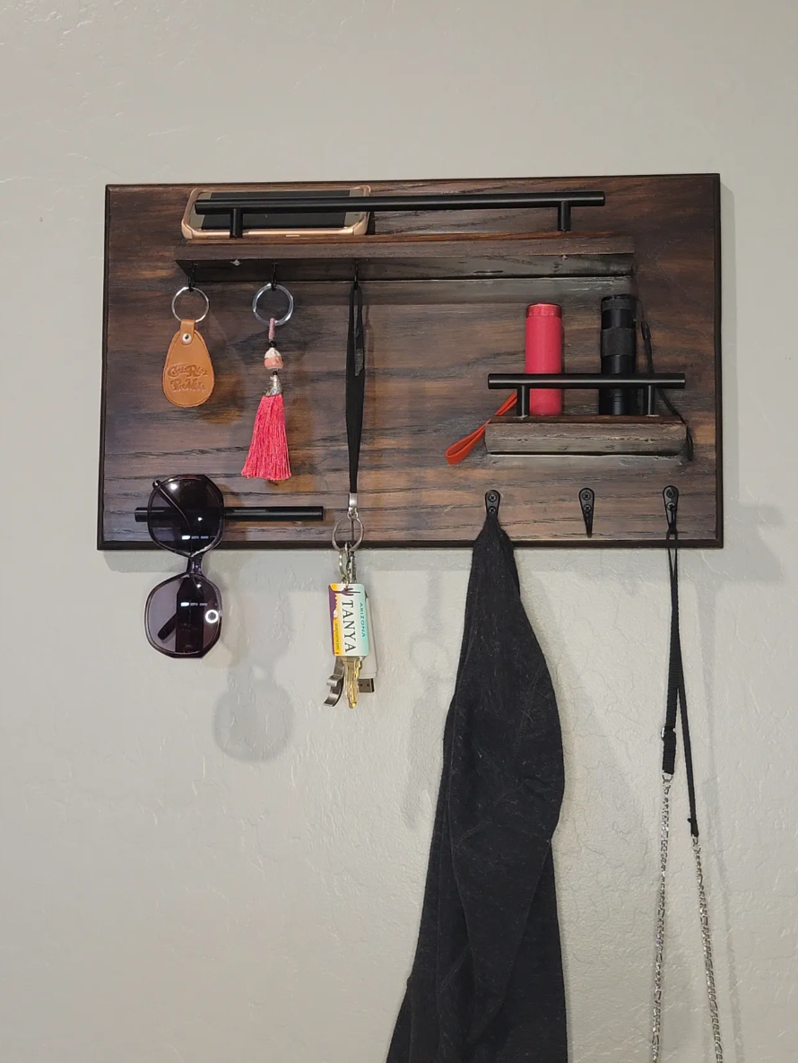 Wooden wall organizer with hooks holding keys, sunglasses, a hoodie, and a lanyard, with small shelves containing water bottles and other items.