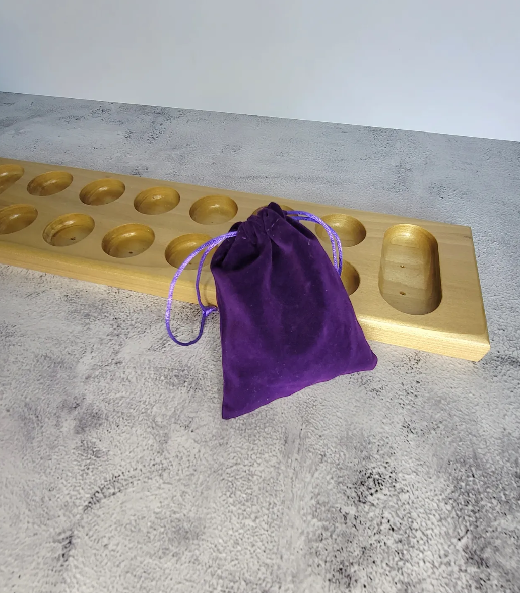 A wooden board with multiple circular holes, a smaller compartment on the side, and a purple velvet drawstring pouch placed on a textured gray surface.