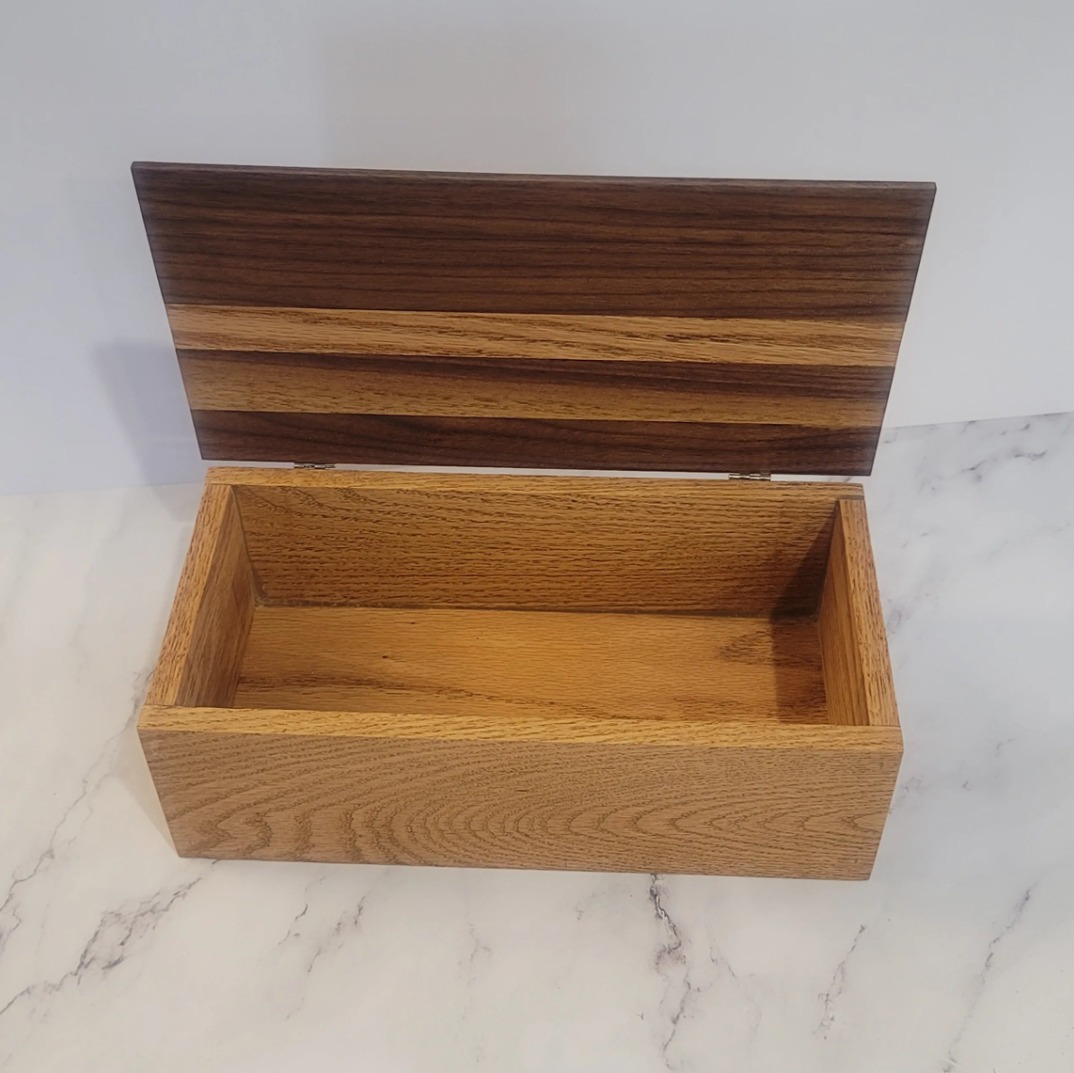 Open wooden box with a hinged lid on a marble surface.
