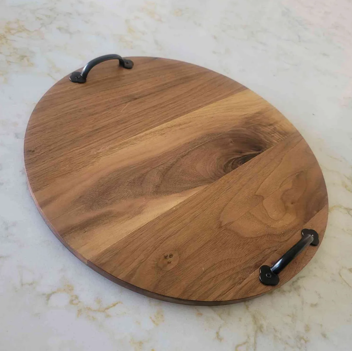 Round wooden tray with black handles on a white surface.