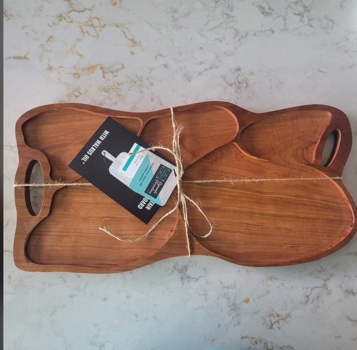 A wooden serving tray with multiple compartments shaped like a paw print, tied with a string and a tag attached.