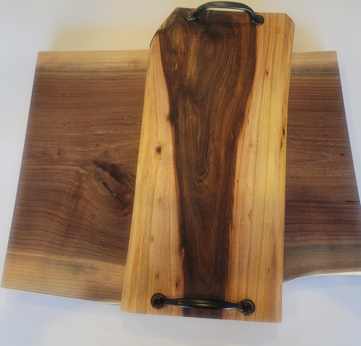 A set of three wooden cutting boards with a handle, made of natural wood, arranged with two boards underneath a larger, butcher-block style board with a handle, on a white surface.