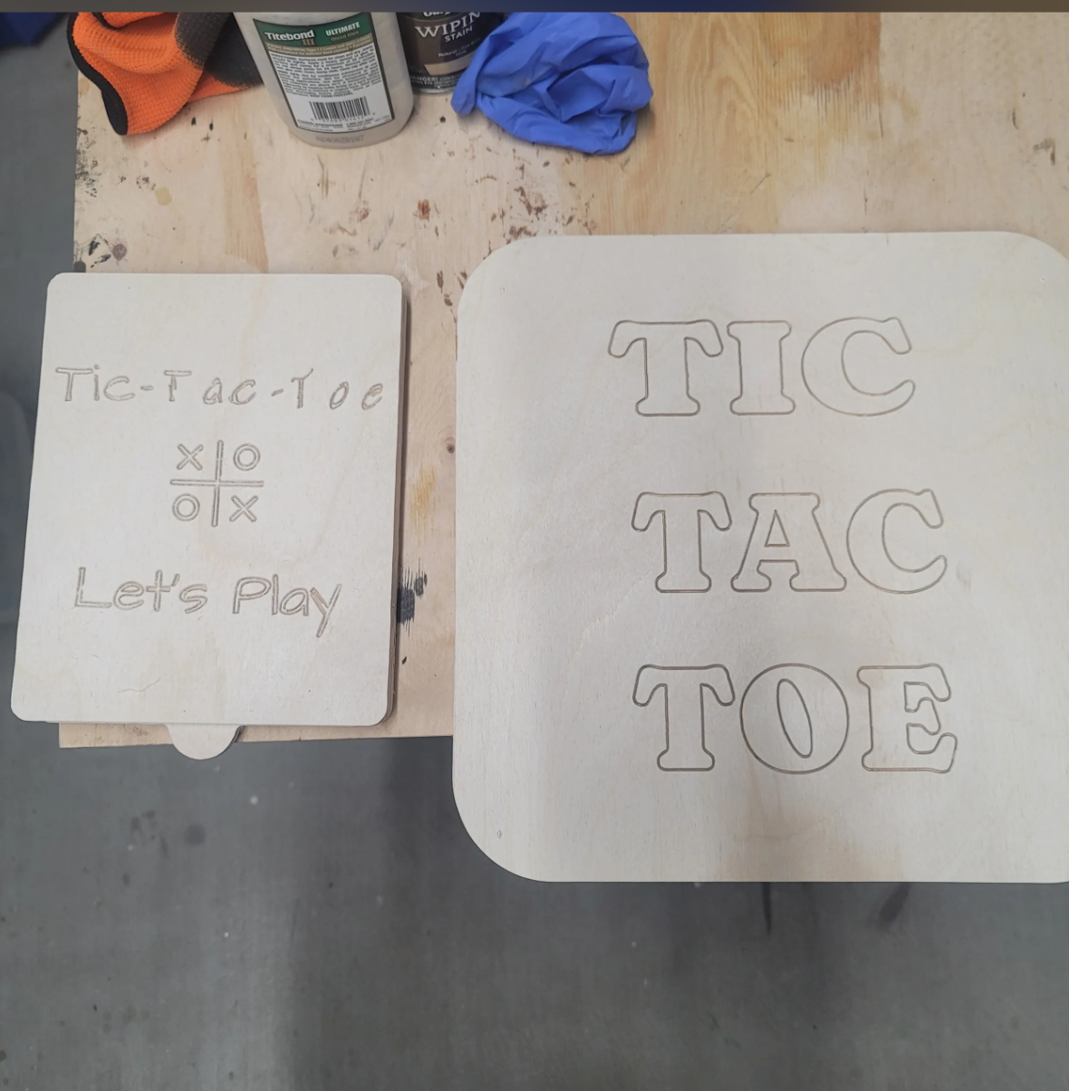 Wooden boards with engraved letters spelling "TIC TAC TOE" and a smaller board with the words "Tic-Tac-Toe" and "Let's Play" along with a tic-tac-toe grid.