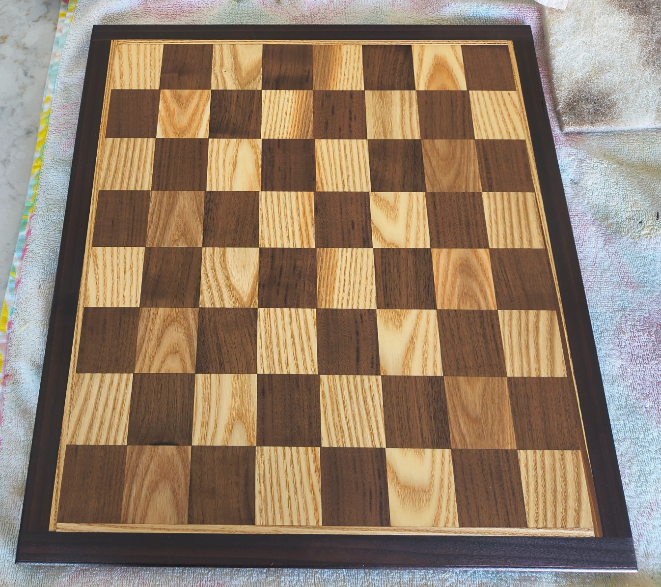 Wooden ash and walnut chessboard with alternating light and dark squares.