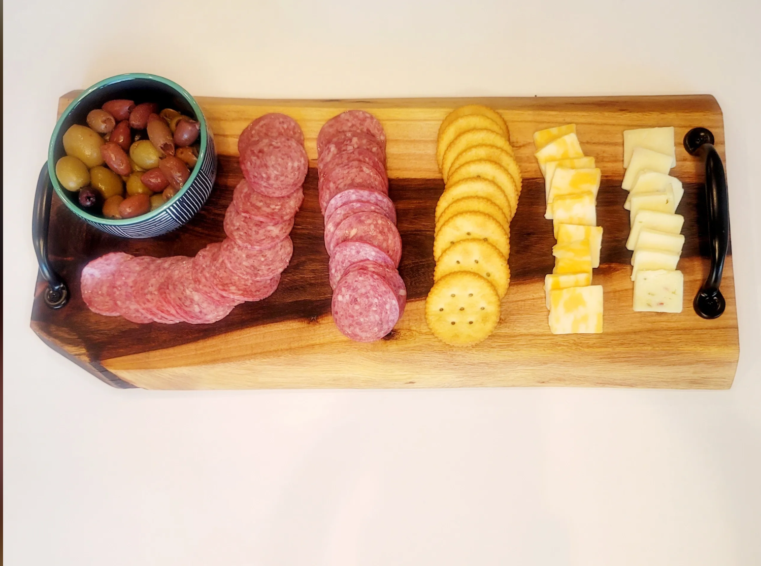 Cheese and charcuterie board with olives, sliced cured meats, round crackers, and sliced cheeses on a wooden serving board.