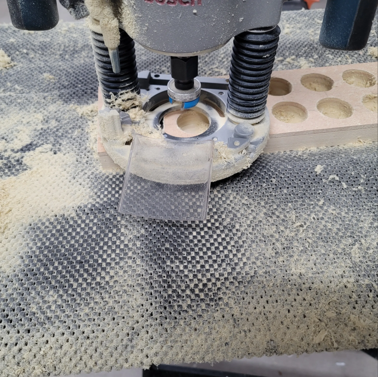 A woodworking router cutting a hole in a piece of poplar wood with dust and debris around it.