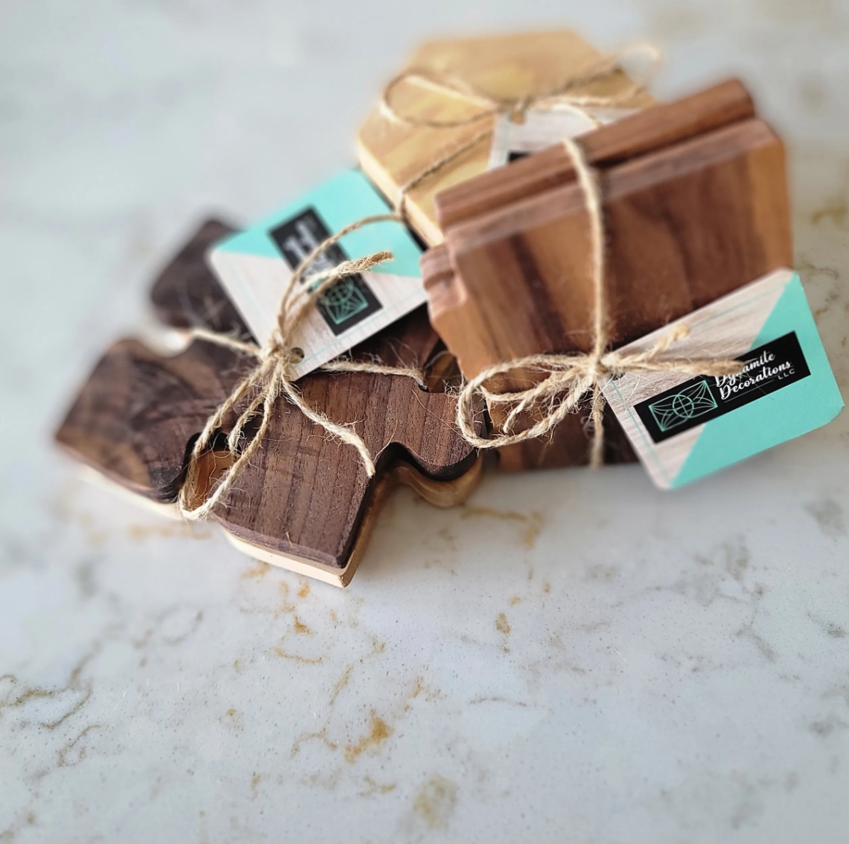 Bundles of wooden coasters tied with twine, labeled with a black and turquoise tag from Basalite Decorations LLC, on a light-colored marble surface.