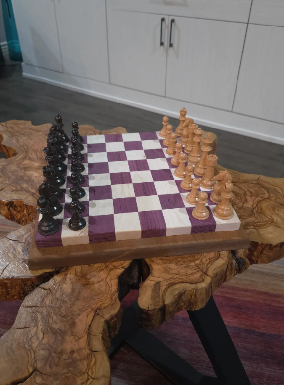 Chessboard with black and natural pieces set up for a game on a rustic wooden table.