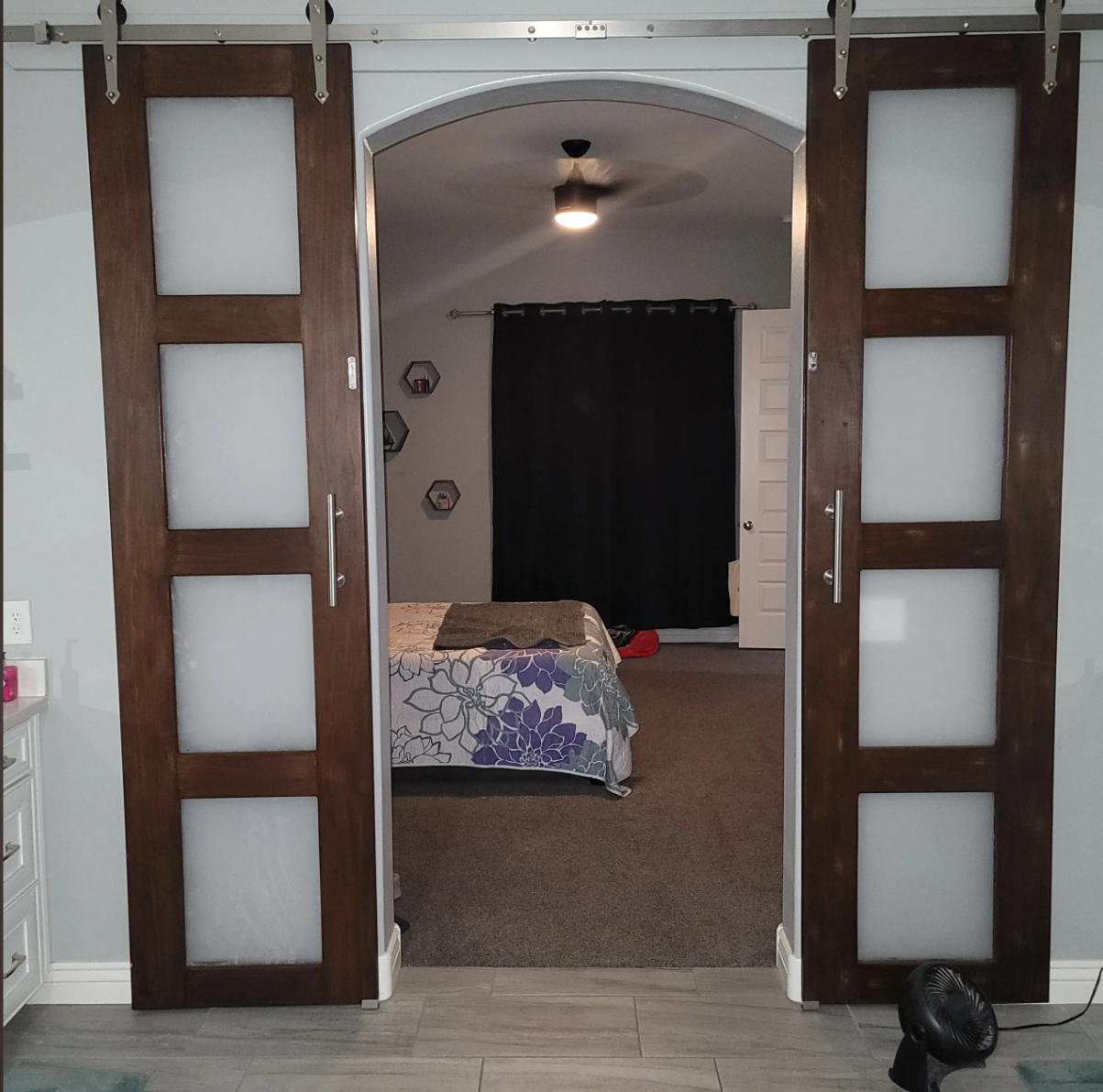 View through sliding frosted glass barn doors into a bedroom with a bed, black curtain, and wall decor.