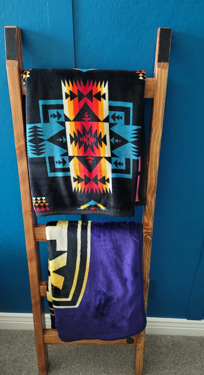 Wooden towel rack with Navajo-style blanket and a towel featuring a sports team logo, set against a blue textured wall.