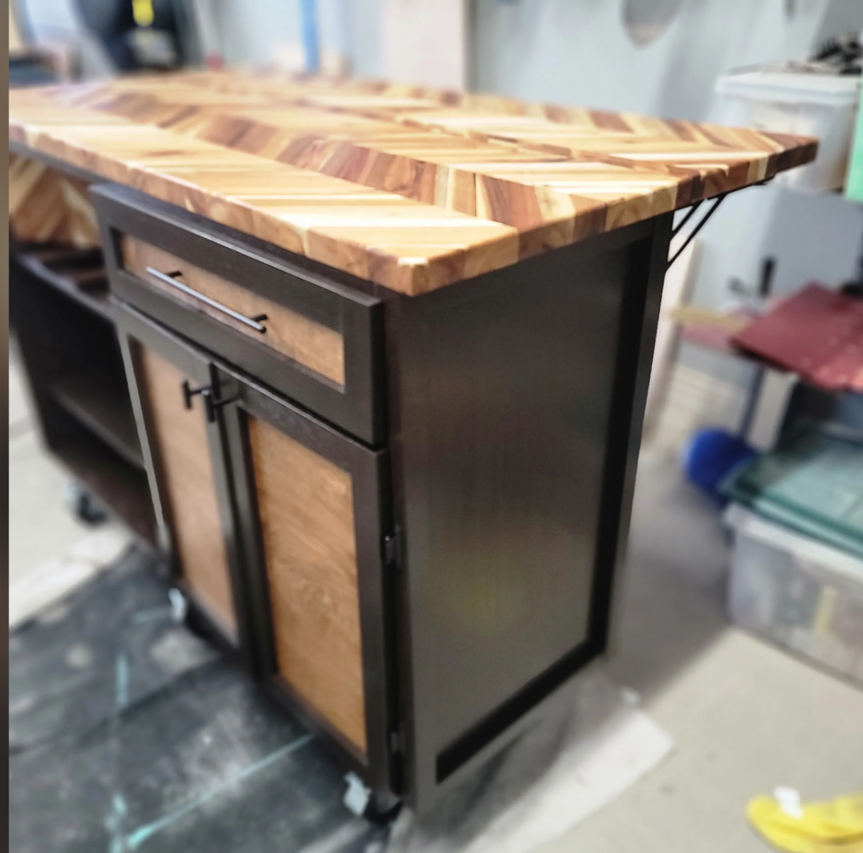 A woodworking cabinet with a black metal frame, wooden doors, and a butcher block top in a workshop.