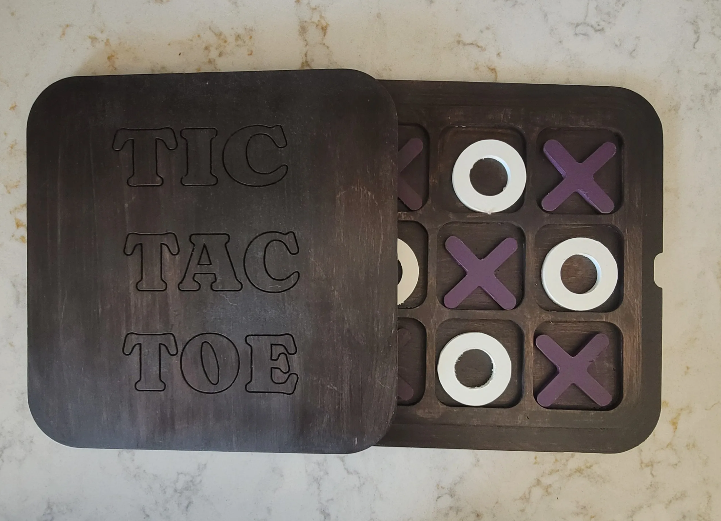 A dark stained wooden Tic Tac Toe game with the top side removed, revealing the game board with black Xs and white O's arranged in a winning pattern on a light-colored surface.