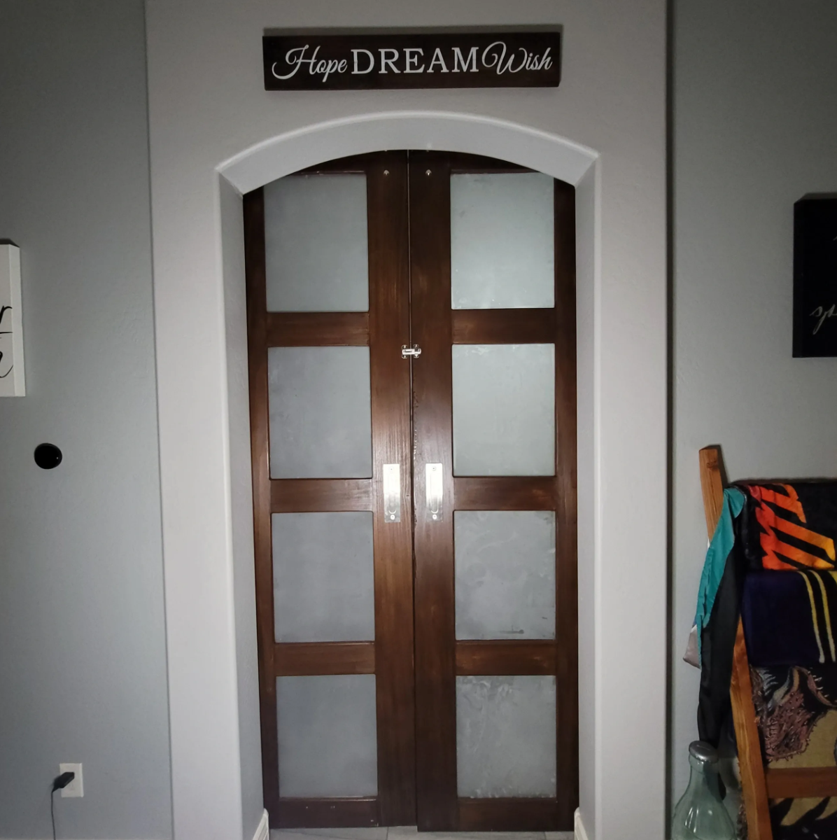 Wooden double doors with frosted glass panels in a home interior, above is a sign that says 'Hope Dream Wish'.