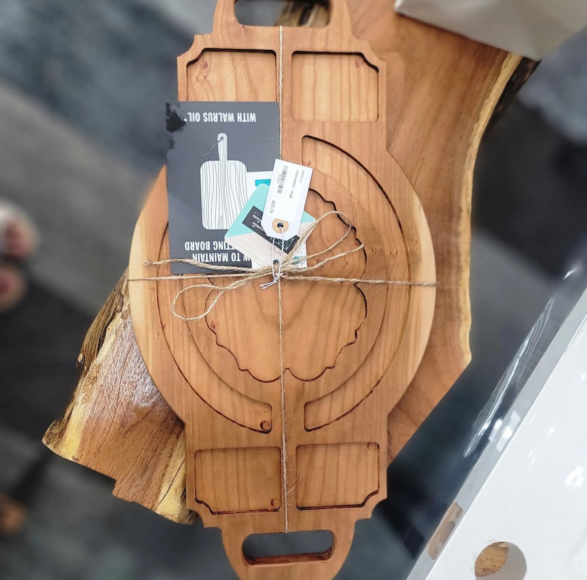 A wooden cutting board shaped like a leaf with a carved flower design in the center, tied with string and tags attached.
