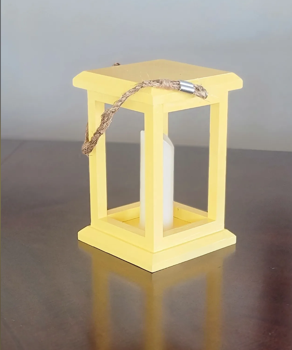 A small yellow wooden lantern with a white pillar candle inside and a twisted brown rope draped over the top.