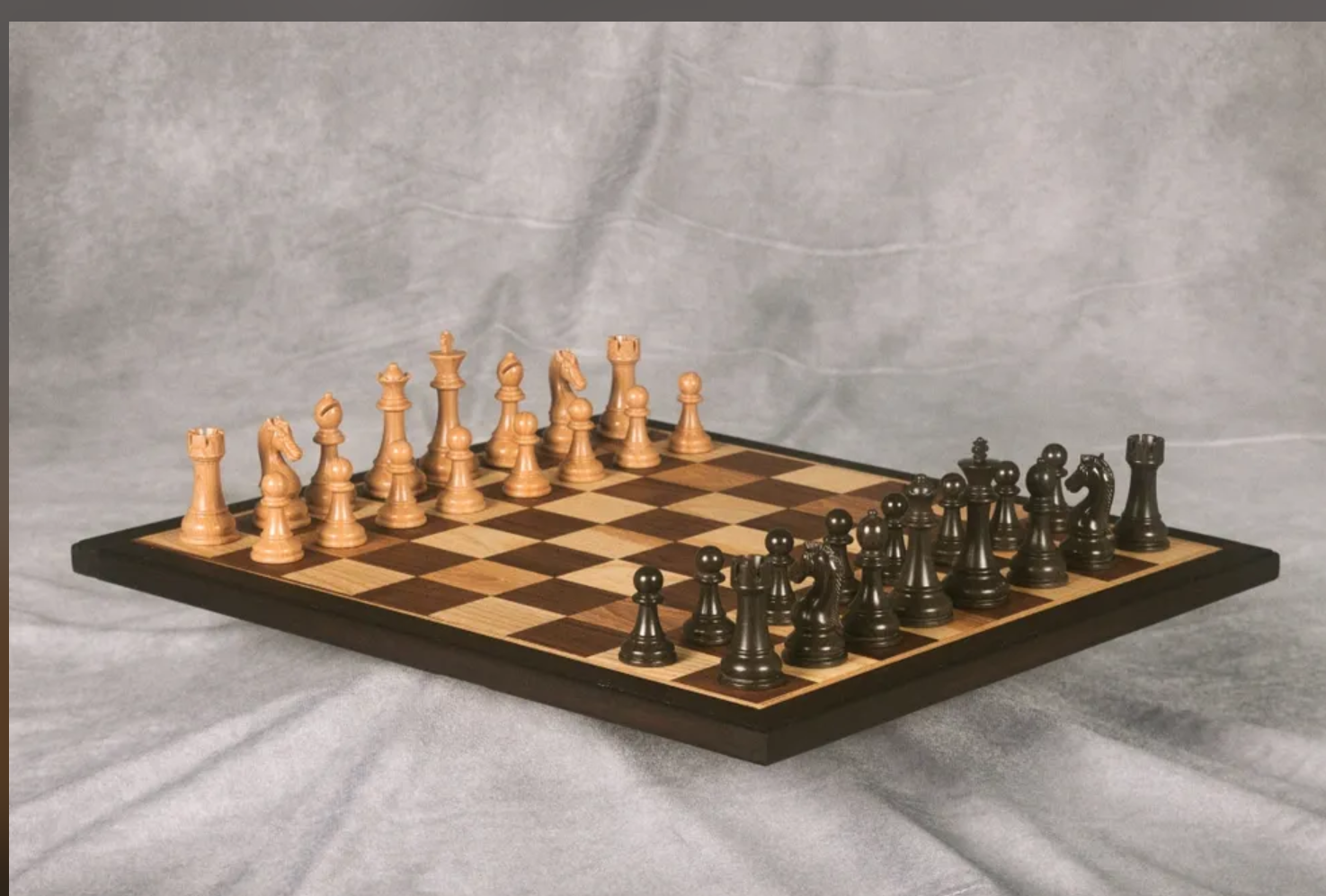 Chessboard with white and black chess pieces arranged in starting positions, on a gray fabric surface.