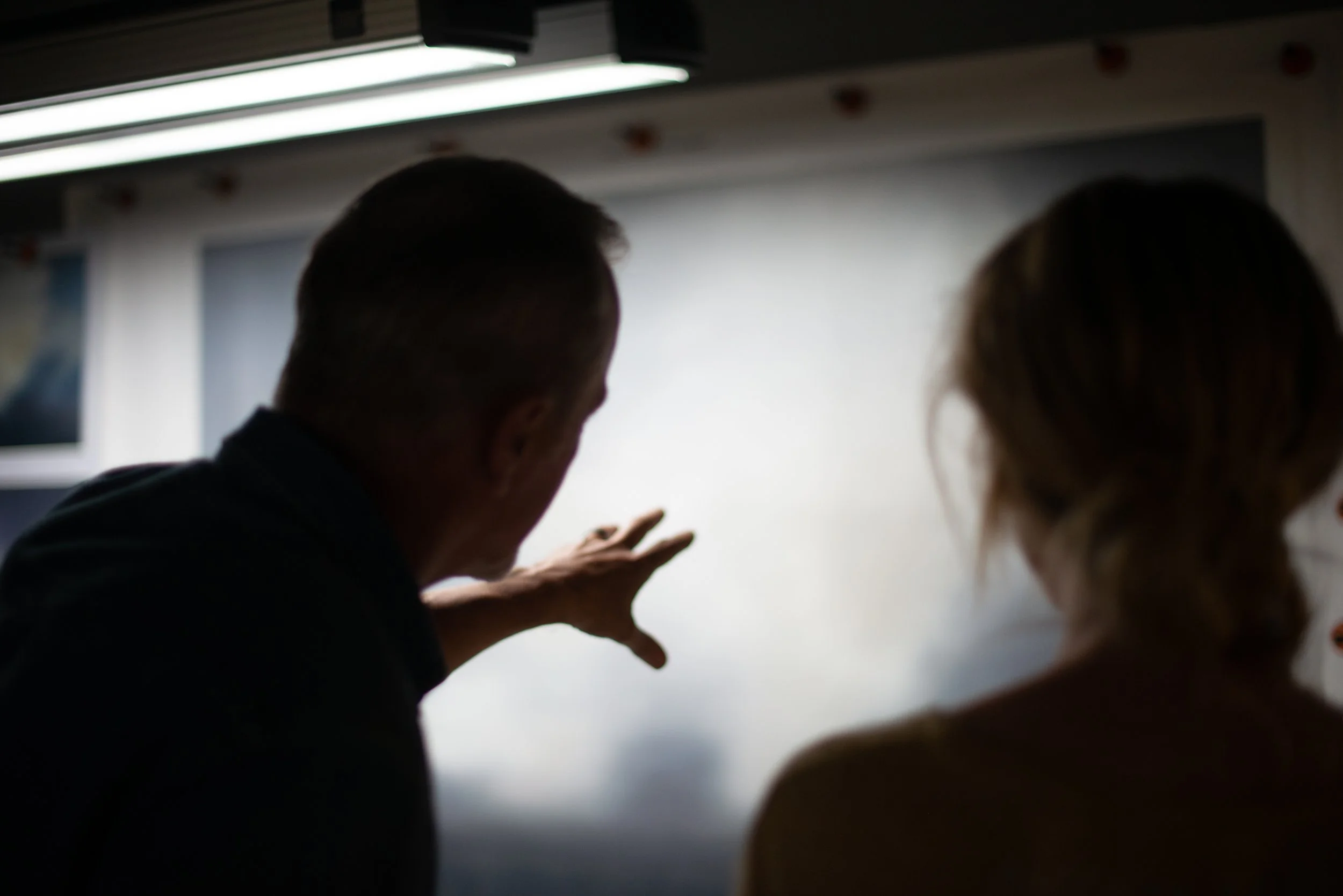 Silhouetted artist looking over artwork replications with Portia de Rossi at General Public headquarters. 