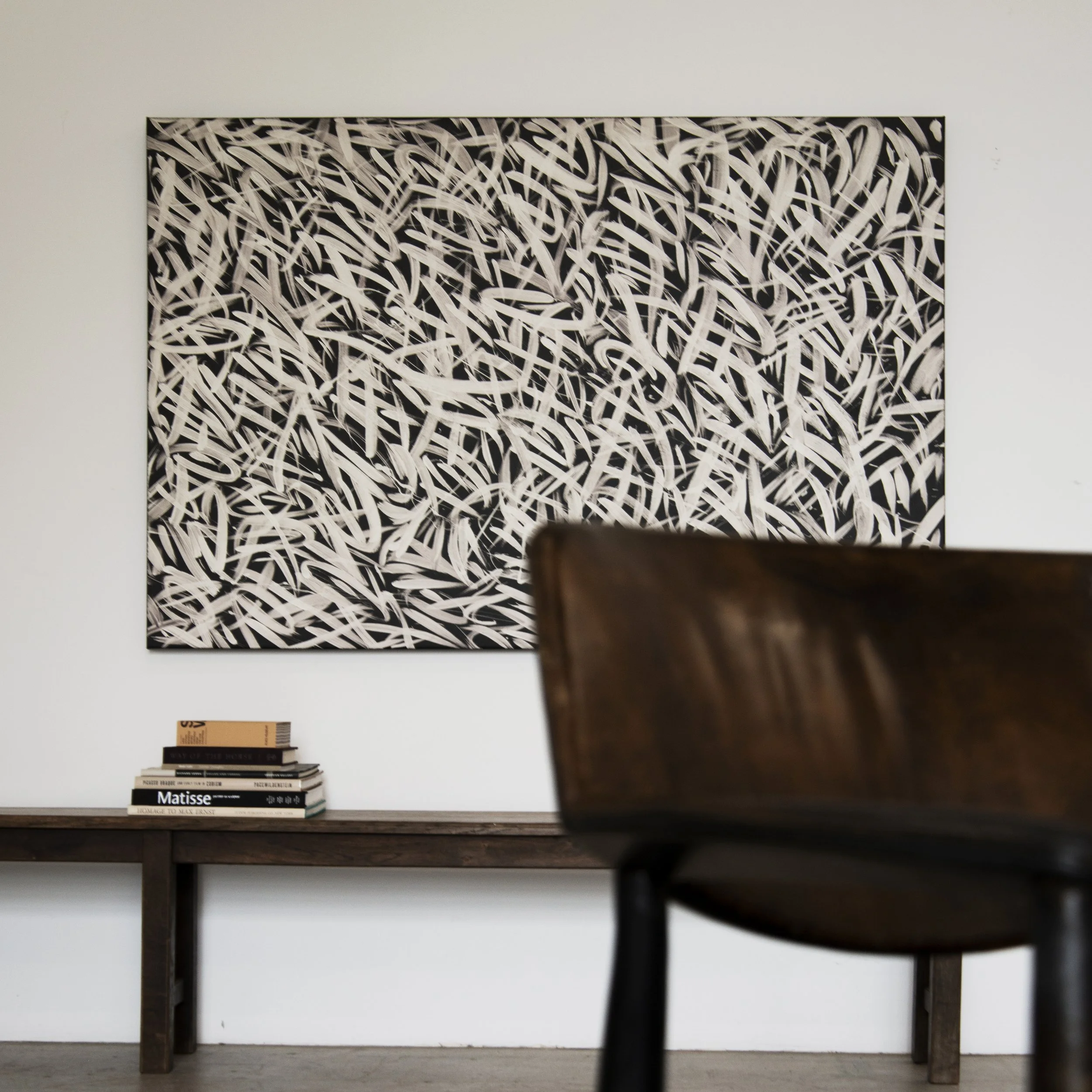 A large abstract black and white painting with swirling lines on a white gallery wall.