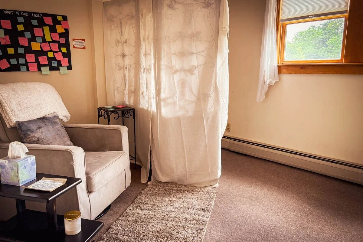 The Prayer Room at The Living Room, an armchair beside a sheer curtain divider with a journal and tissue box