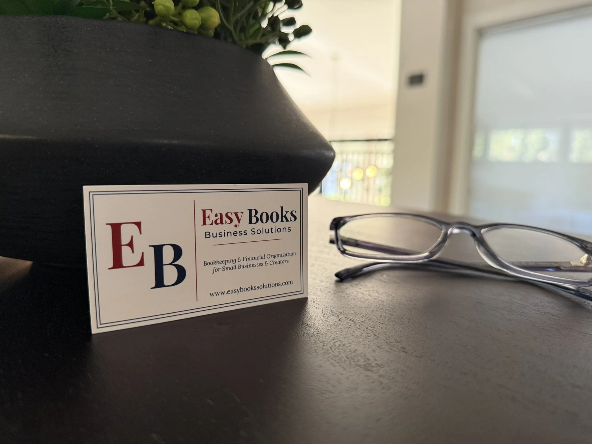 Close-up of a black book with a business solutions label, a pair of glasses, and a plant in the background near a window.