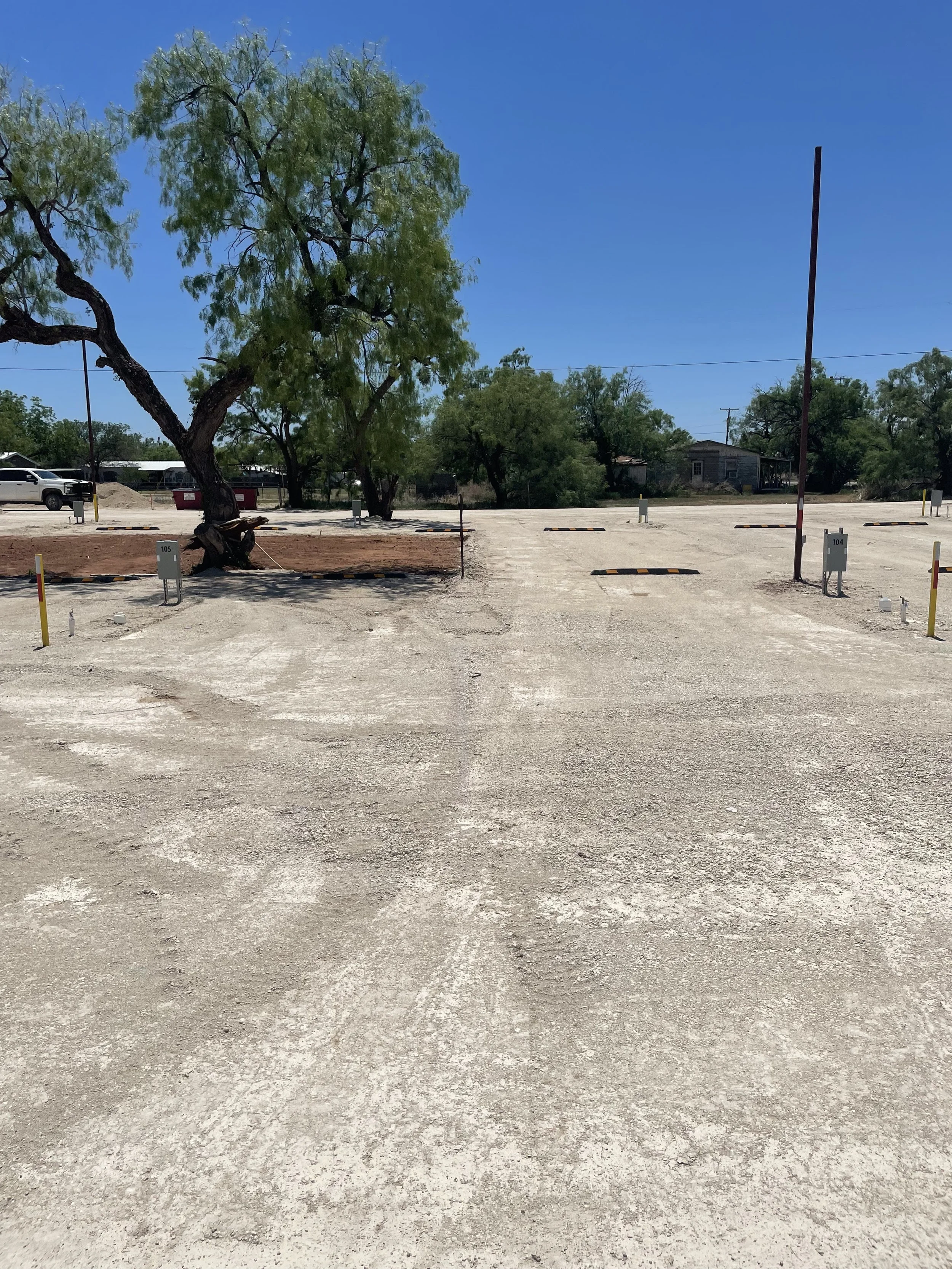 A parking lot with trees, a parked white truck, and a clear blue sky.