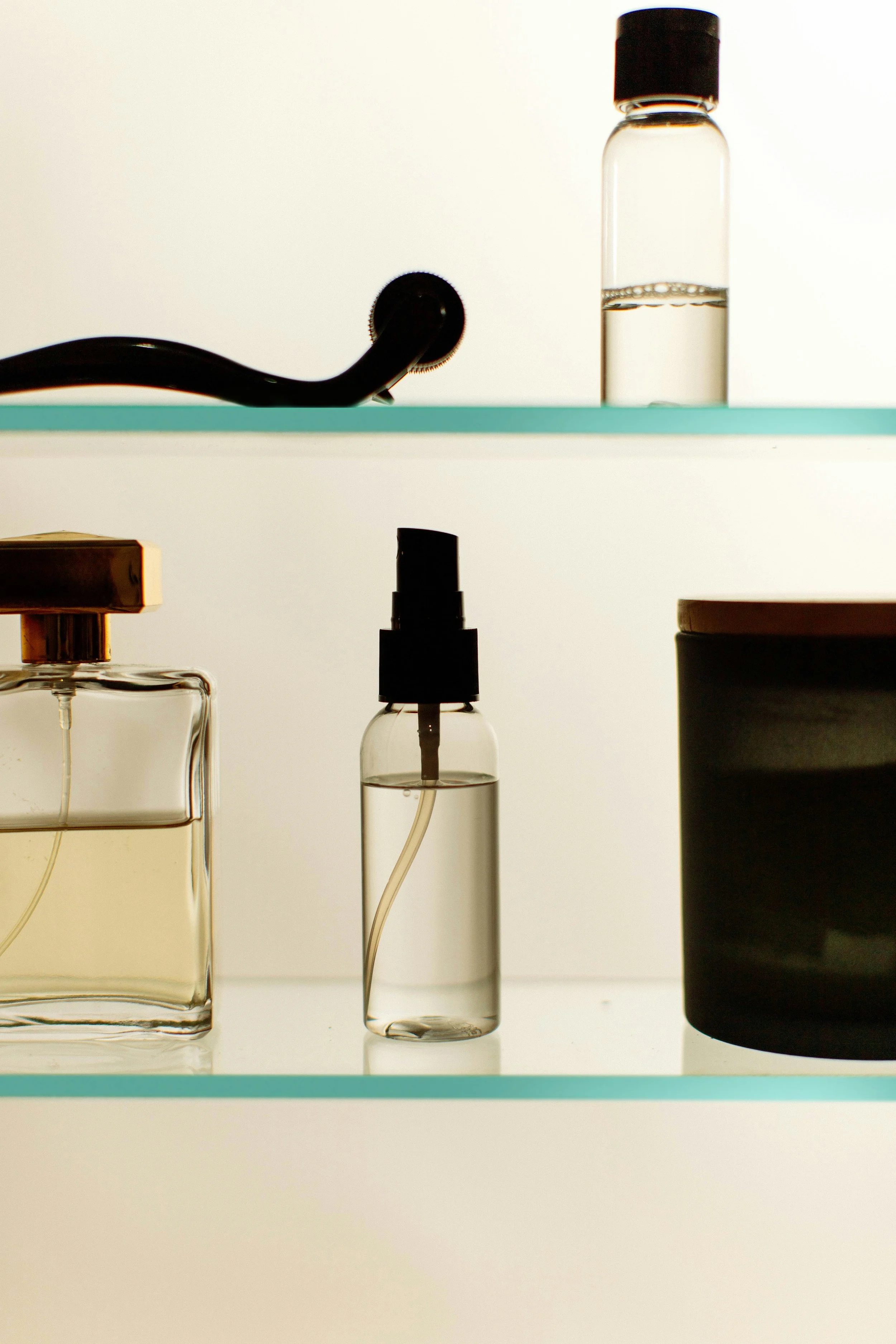 Various laboratory glass bottles and containers, some with liquids and some empty, placed on a glass shelf with a white background.