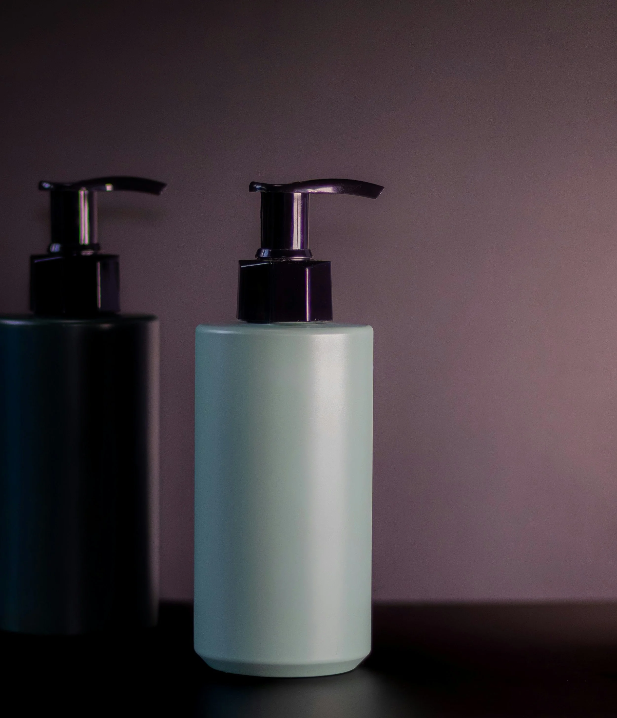 A white plastic bottle with a purple pump dispenser on top, set against a dark background.