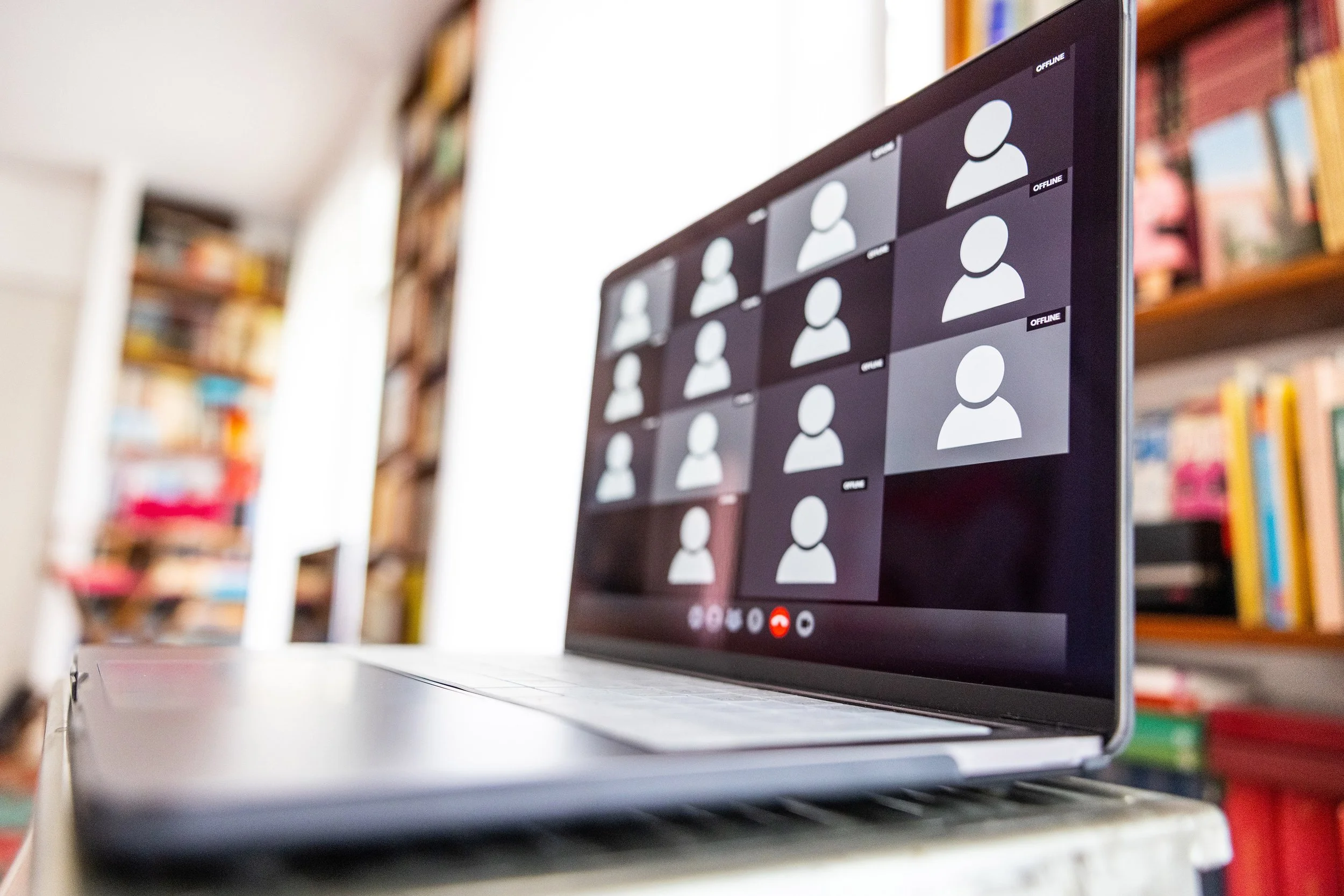 Laptop on a desk showing a video call, bookshelves behind.