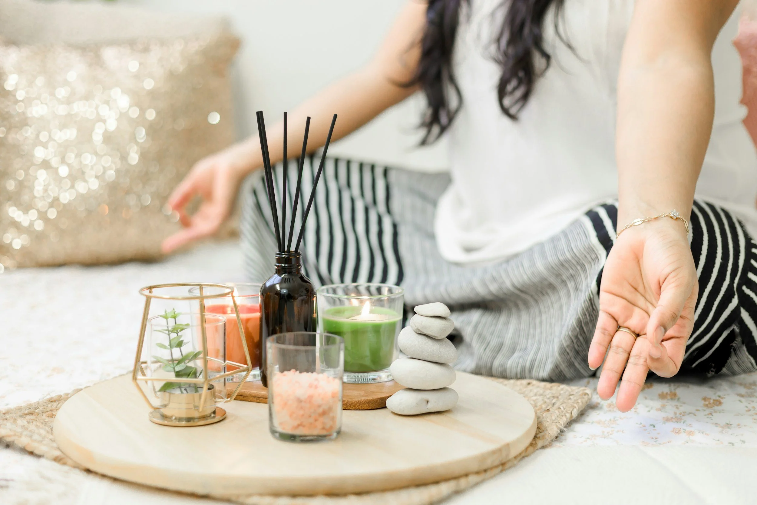 A woman arranging candles and stones on a round wooden tray, with incense sticks and decorative items nearby.