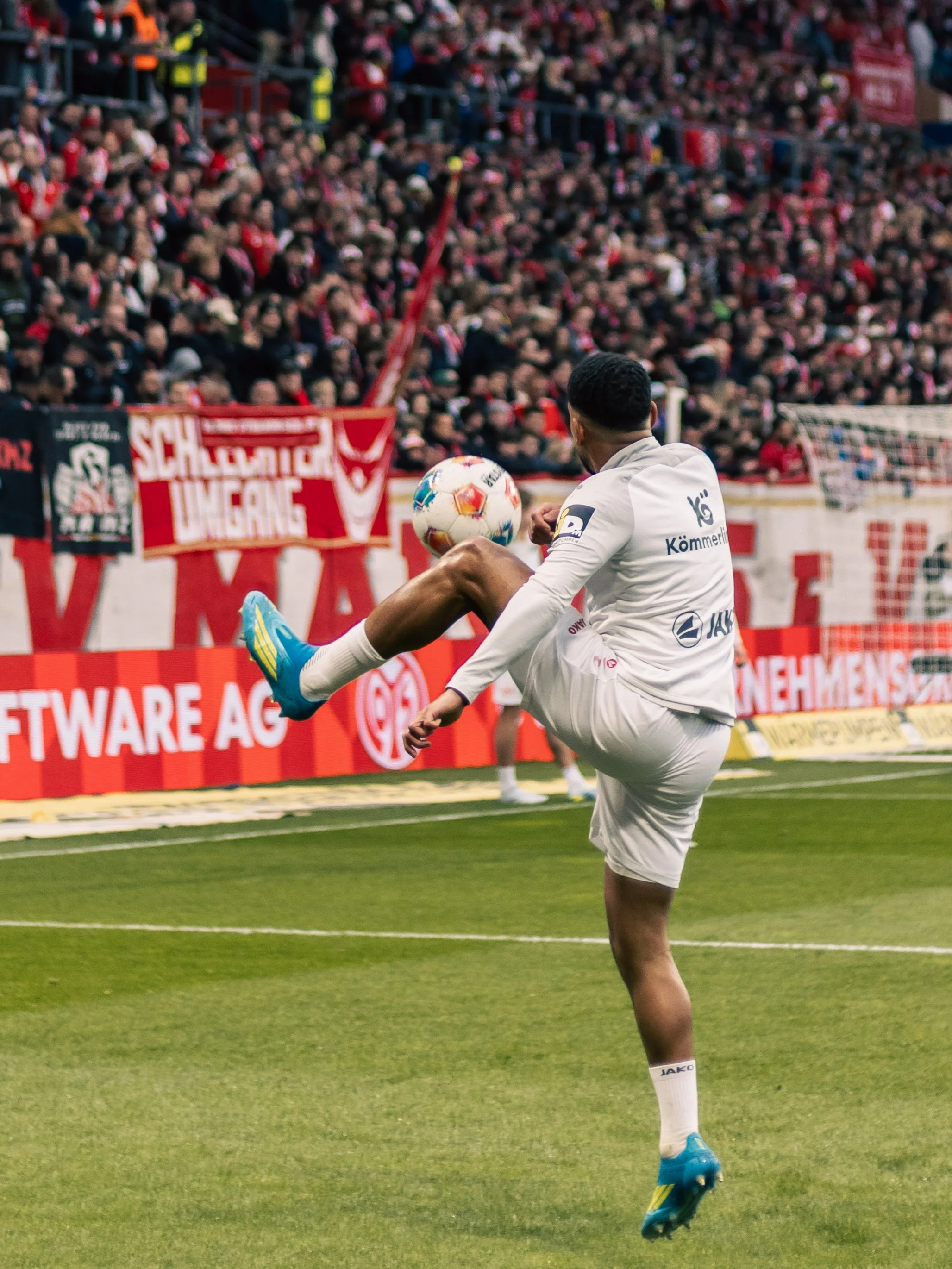 Fußballspieler vom 1. FSV Mainz 05 in weißem Trikot führt den Ball während eines Spiels vor einem großen Publikum auf einem Fußballfeld. Sportfotografie beim 1. FSV Mainz 05 in der Bundesliga.