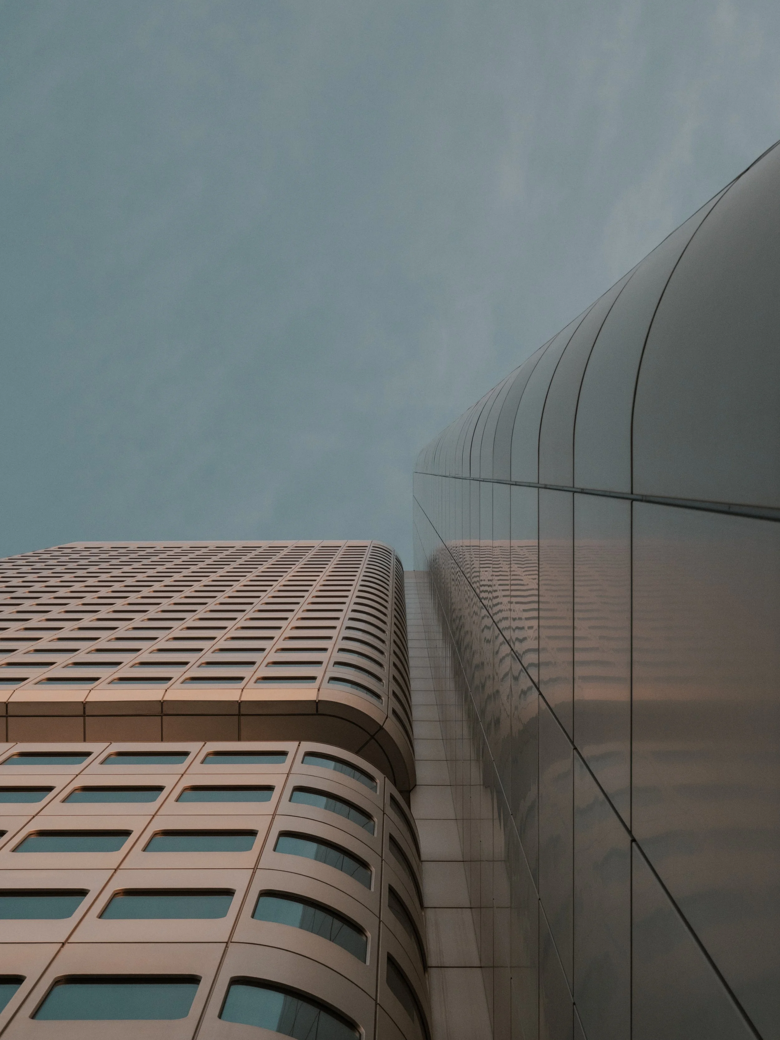 Aufnahme von unten eines modernen Hochhauses in Frankfurt am Main mit gläsernen Fassaden, bei bewölktem Himmel.