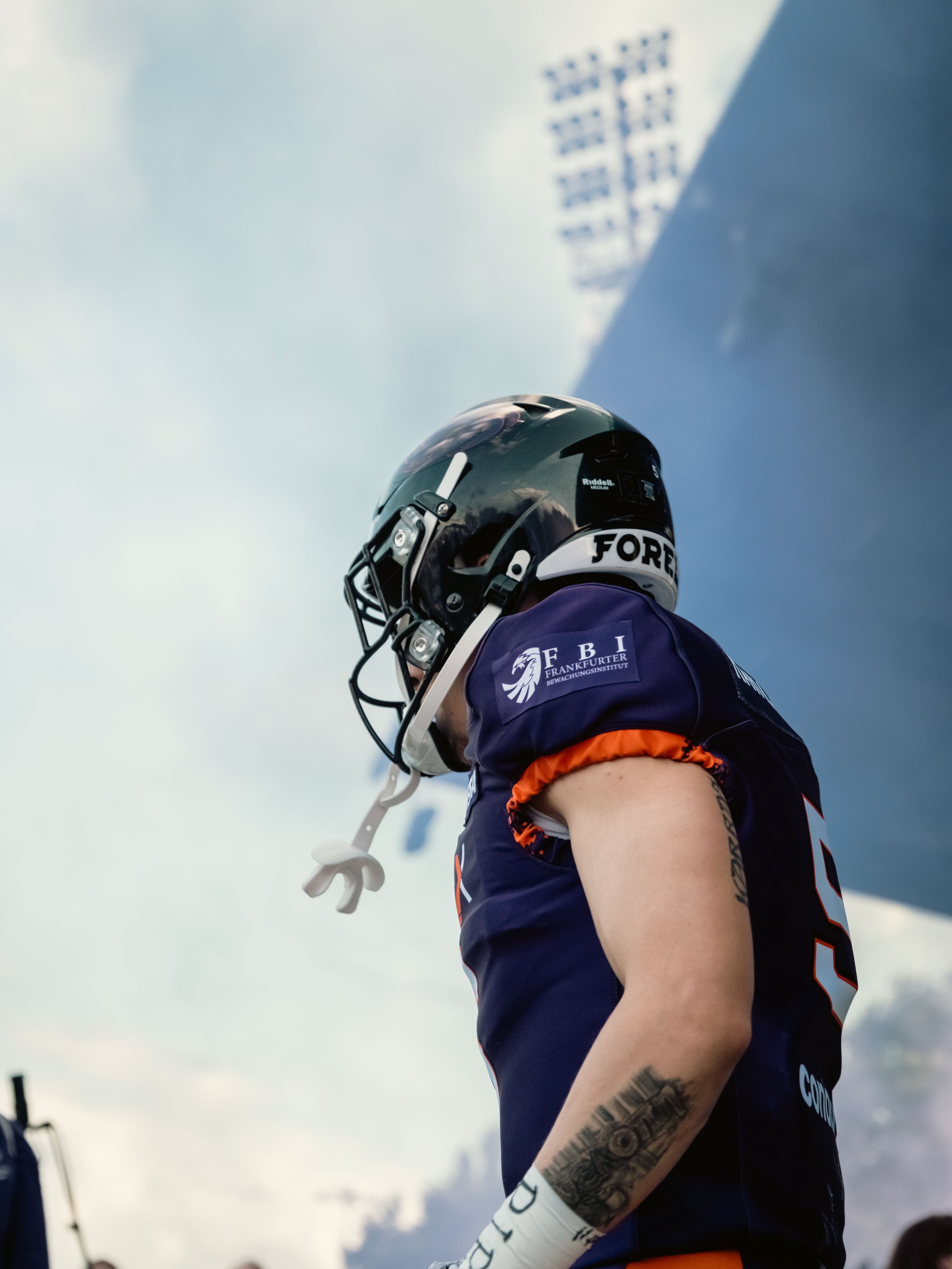 Ein American-Football-Spieler in lila Uniform mit Logo auf dem Ärmel, trug einen schwarzen Helm und weißen Handschuh, schaut nach oben gegen bewölkten Himmel. Einlauf beim Spiel. Sportfotografie bei der Frankfurt Galaxy.