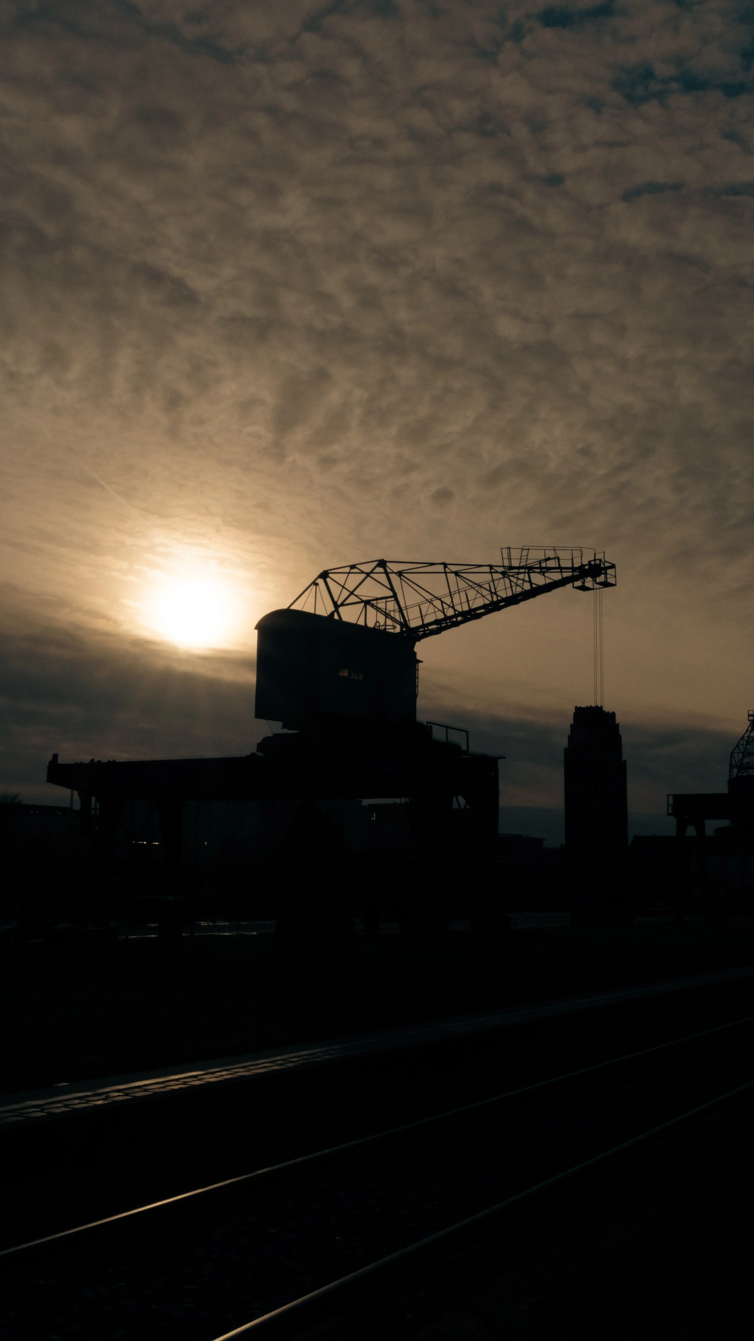 Silhouette einer Baustellenkran bei Sonnenuntergang unter einem bewölkten Himmel.