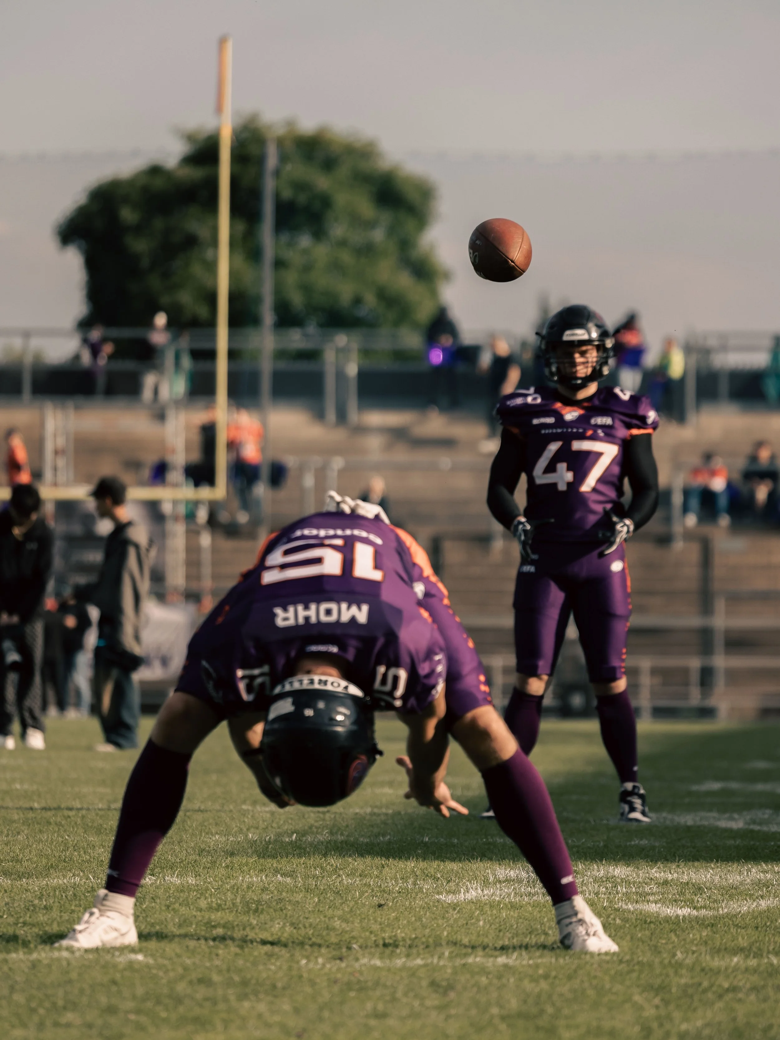 American Football-Spieler der Frankfurt Galaxy in lila Uniformen während eines Spiels, Ball in der Luft, mit einem Stadion im Hintergrund. Sportfotografie in Frankfurt.