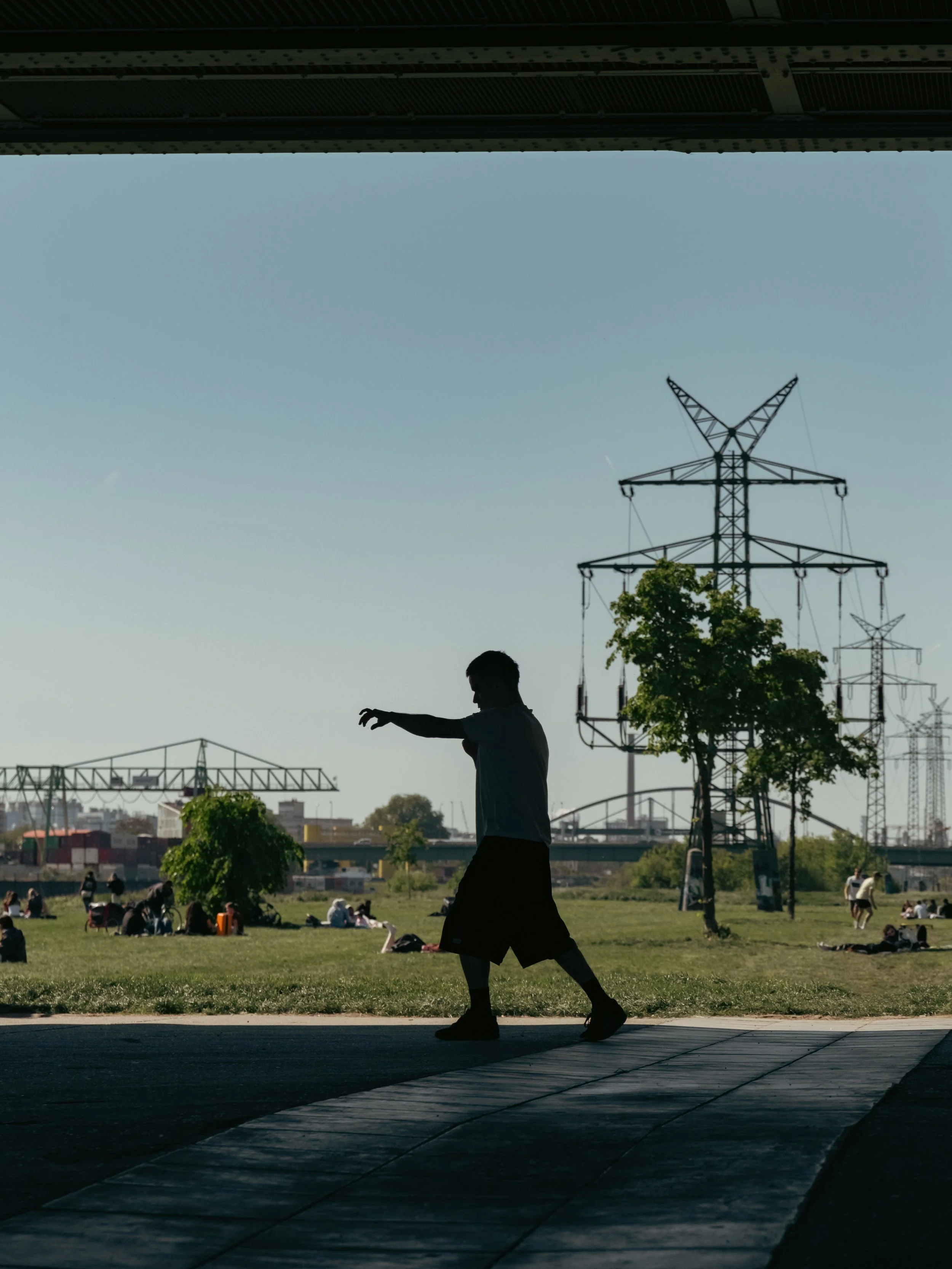 Ein Junge macht Sport in Form von Box-Übungen in einem Park,  im Hintergrund sind Menschen, Bäume und Strommasten sichtbar.
