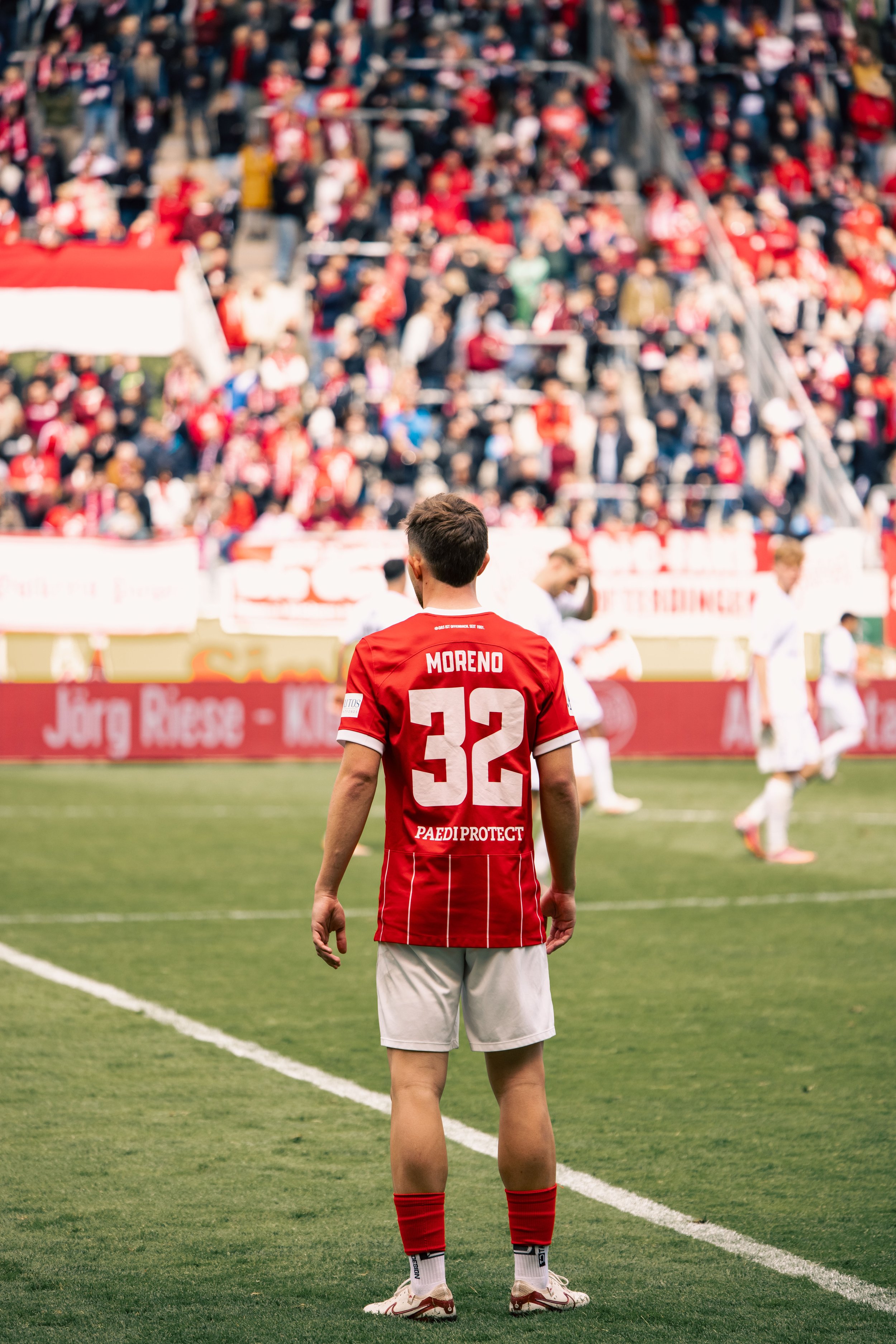 Fußballspieler mit Rückennummer 32 steht auf dem Spielfeld während eines Spiels, im Hintergrund jubelndes Publikum.
