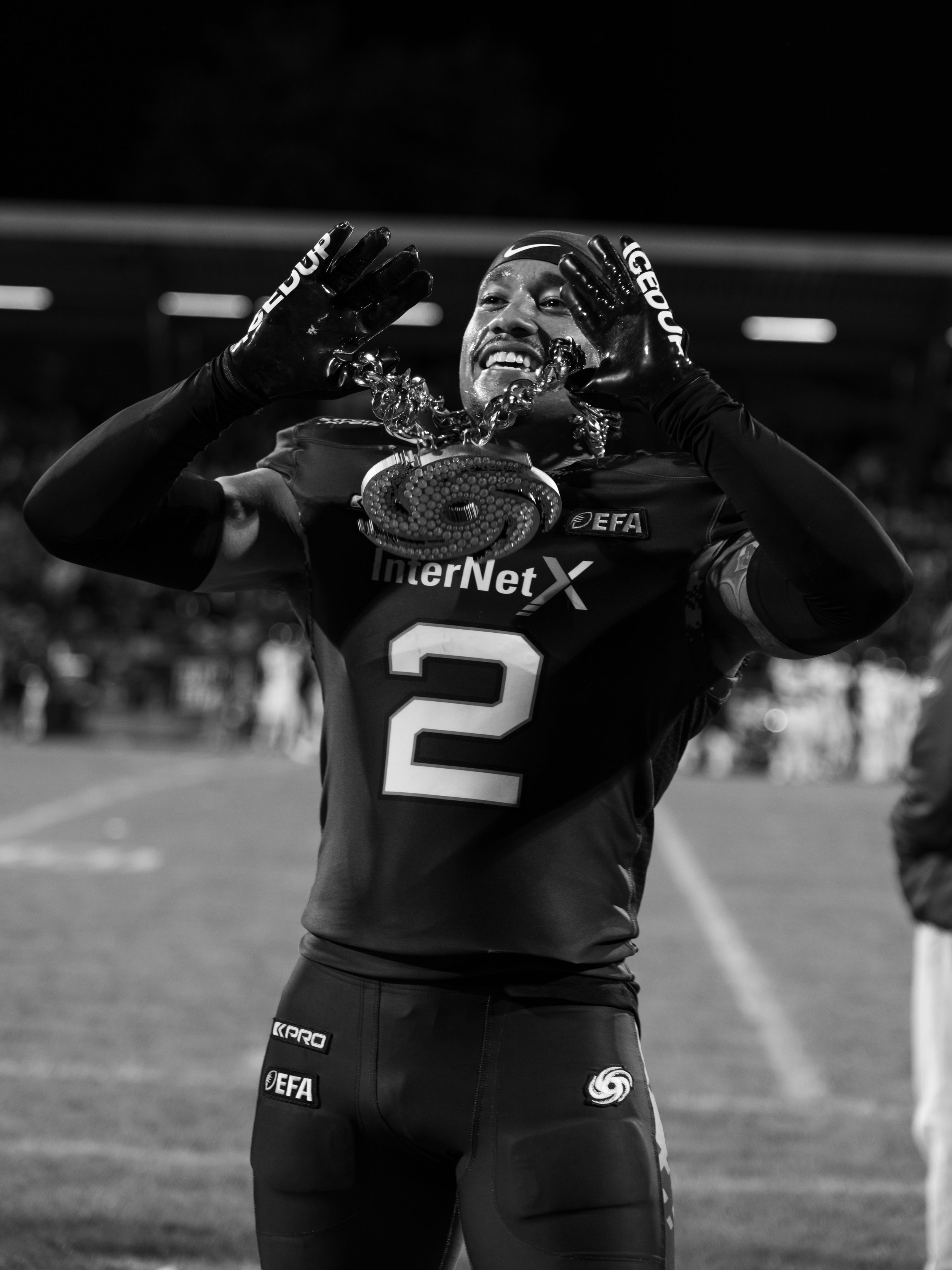Schwarz-Weiß-Foto eines American Football Spielers mit Frankfurt Galaxy Kette, der im Stadion nach einem Wettkampf jubelt. Sportfotografie bei der Frankfurt Galaxy.
