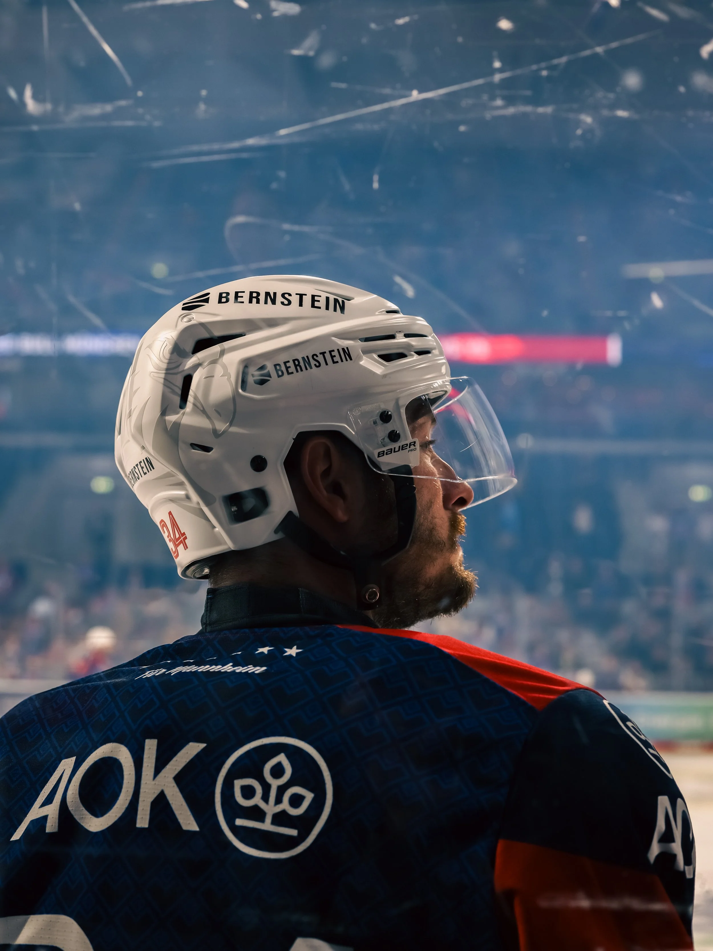 Eishockeyspieler von Adler Mannheim trägt Helm und Blick nach rechts, im Hintergrund das Eisstadion, Sicht auf die Arena während des Spiels. Sport-Fotografie in Mannheim.