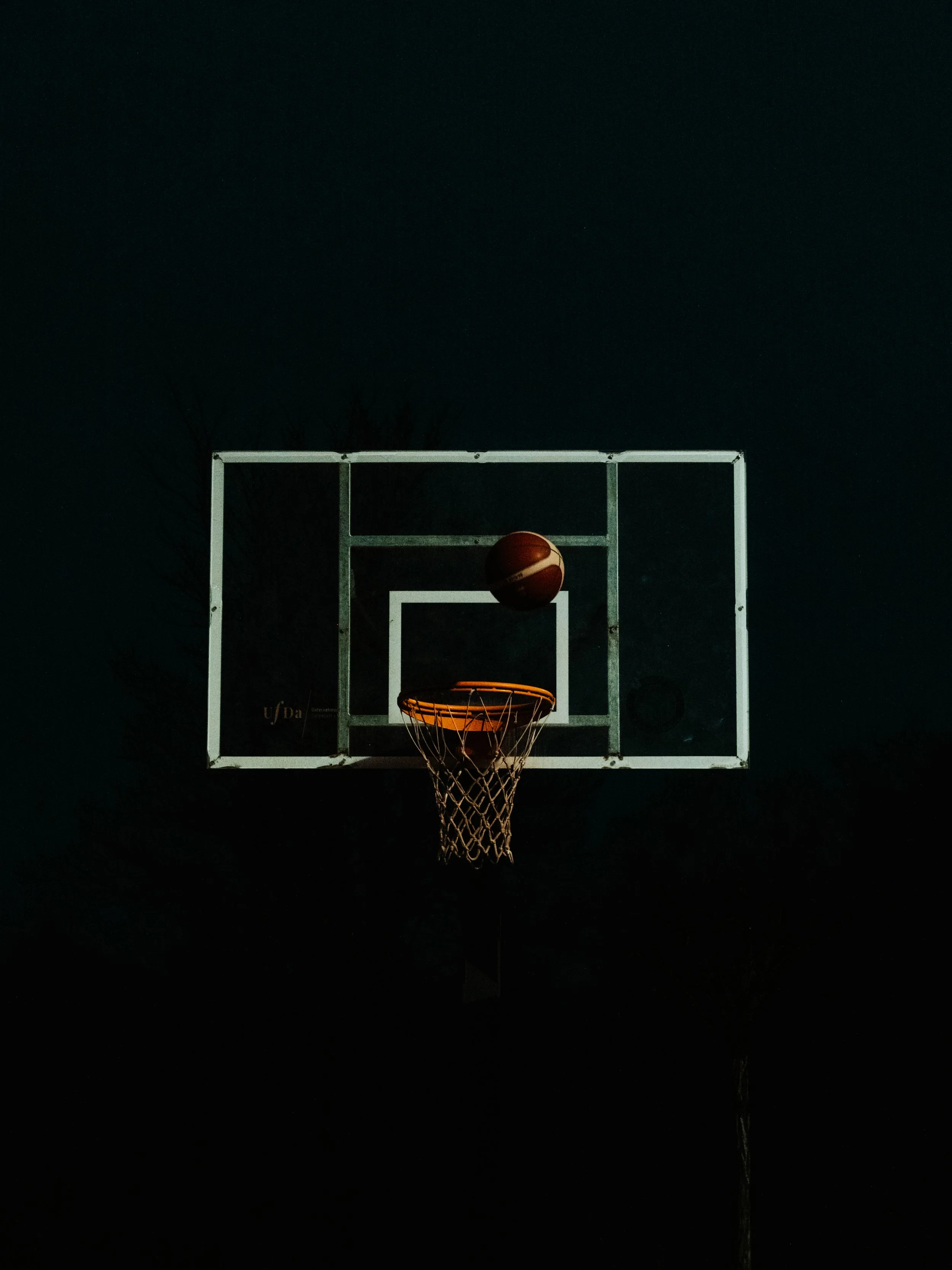 Basketballkorb bei Nacht mit Basketball in der Luft
