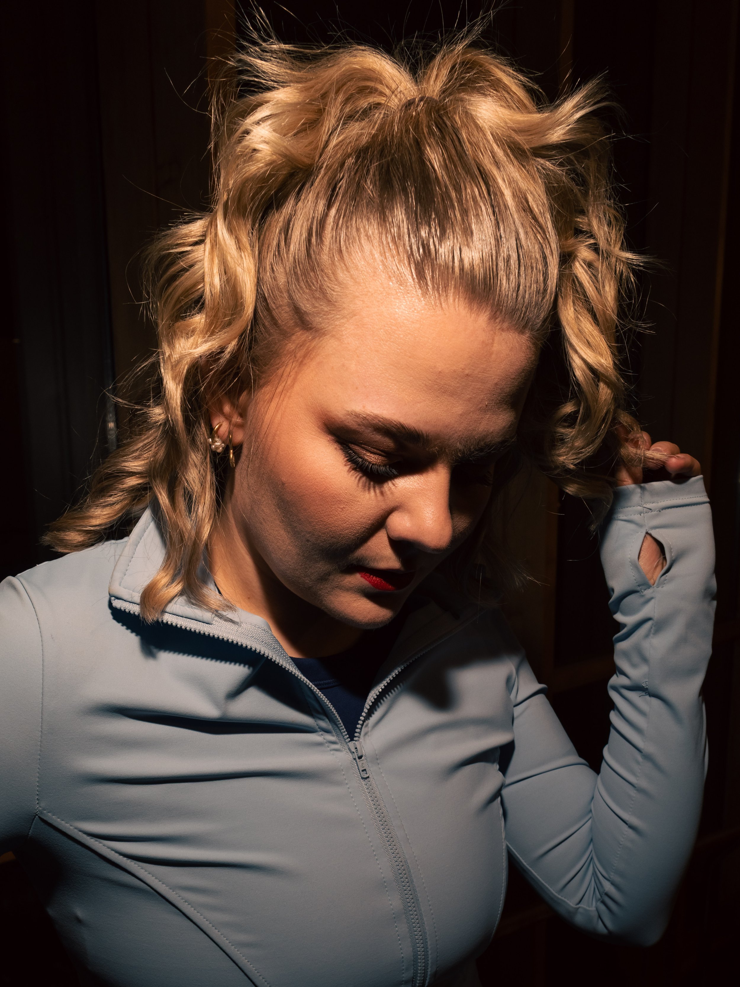 Nahaufnahme einer Frau mit blonden, lockigen Haaren, die ihren Kopf nach unten neigt und die Augen geschlossen hat. Fotografiert mit Blitz.
