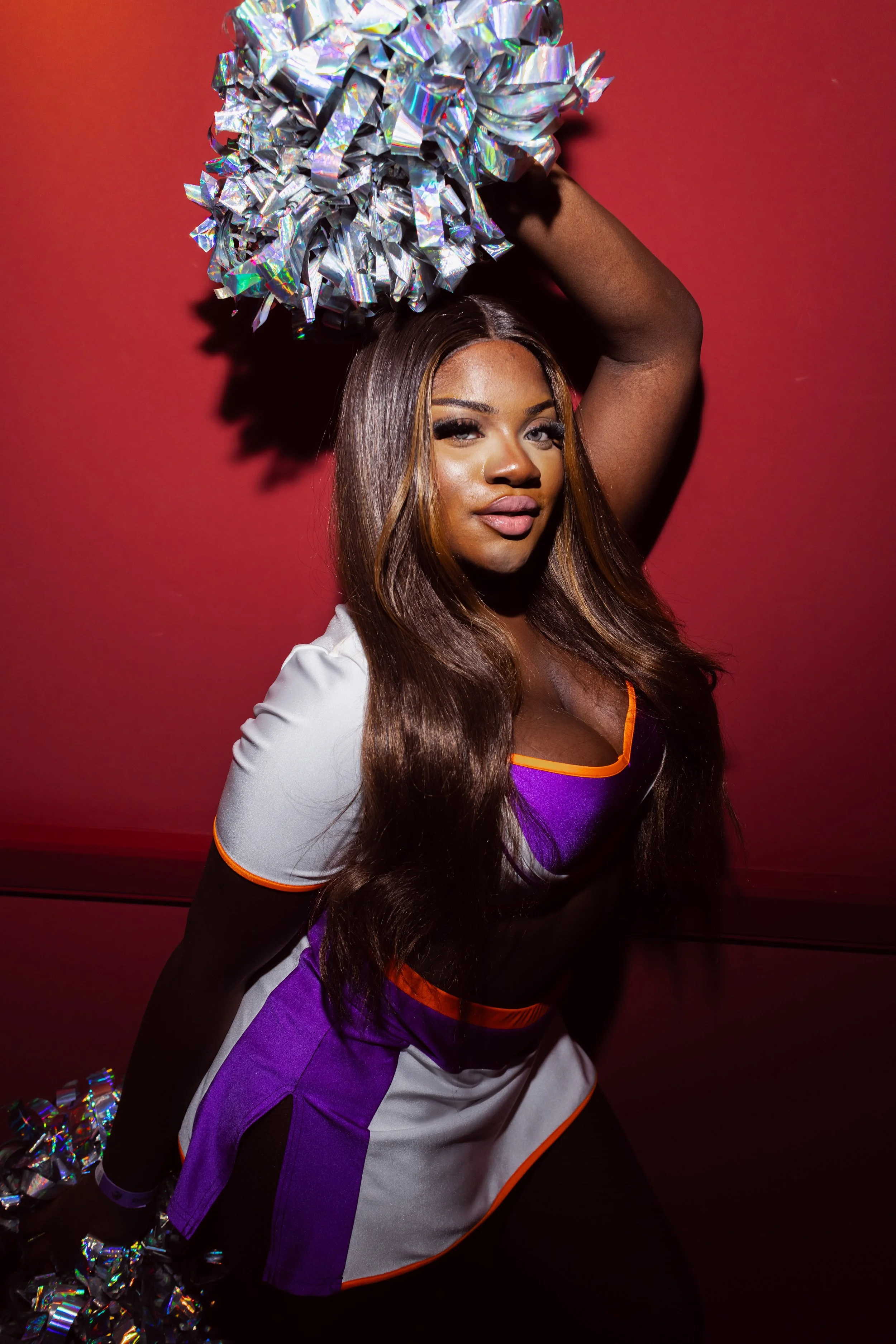 Eine Cheerleaderin posiert mit einem silbrigen Pompon vor einem roten Hintergrund.