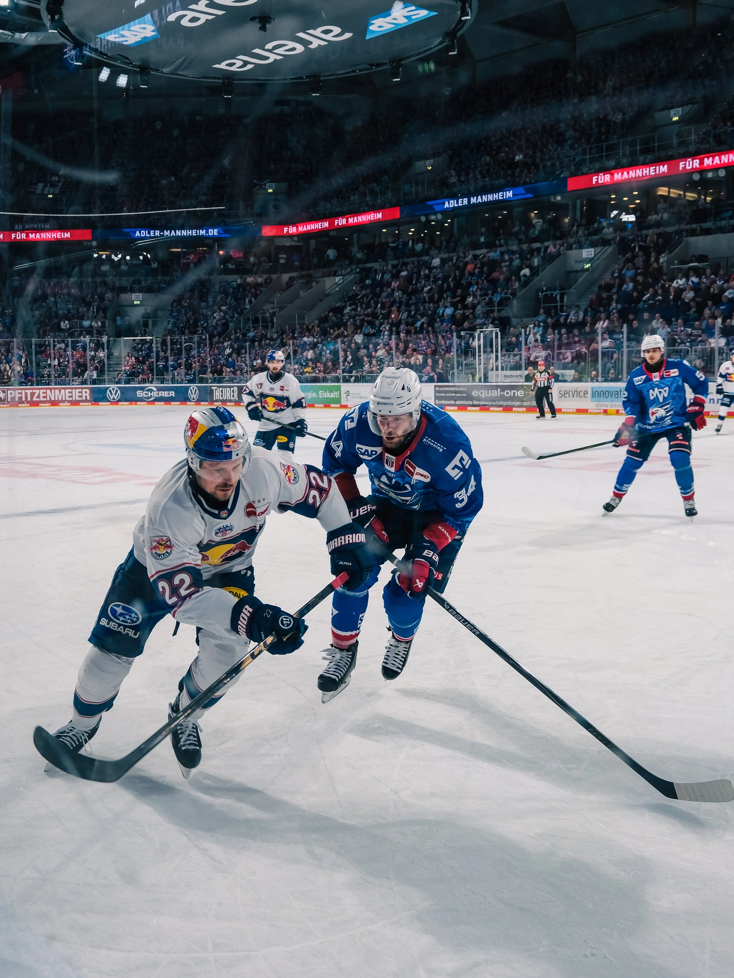 Eishockeyspiel mit Spielern in Aktion auf der Eisbahn in einem Stadion voller Zuschauer.