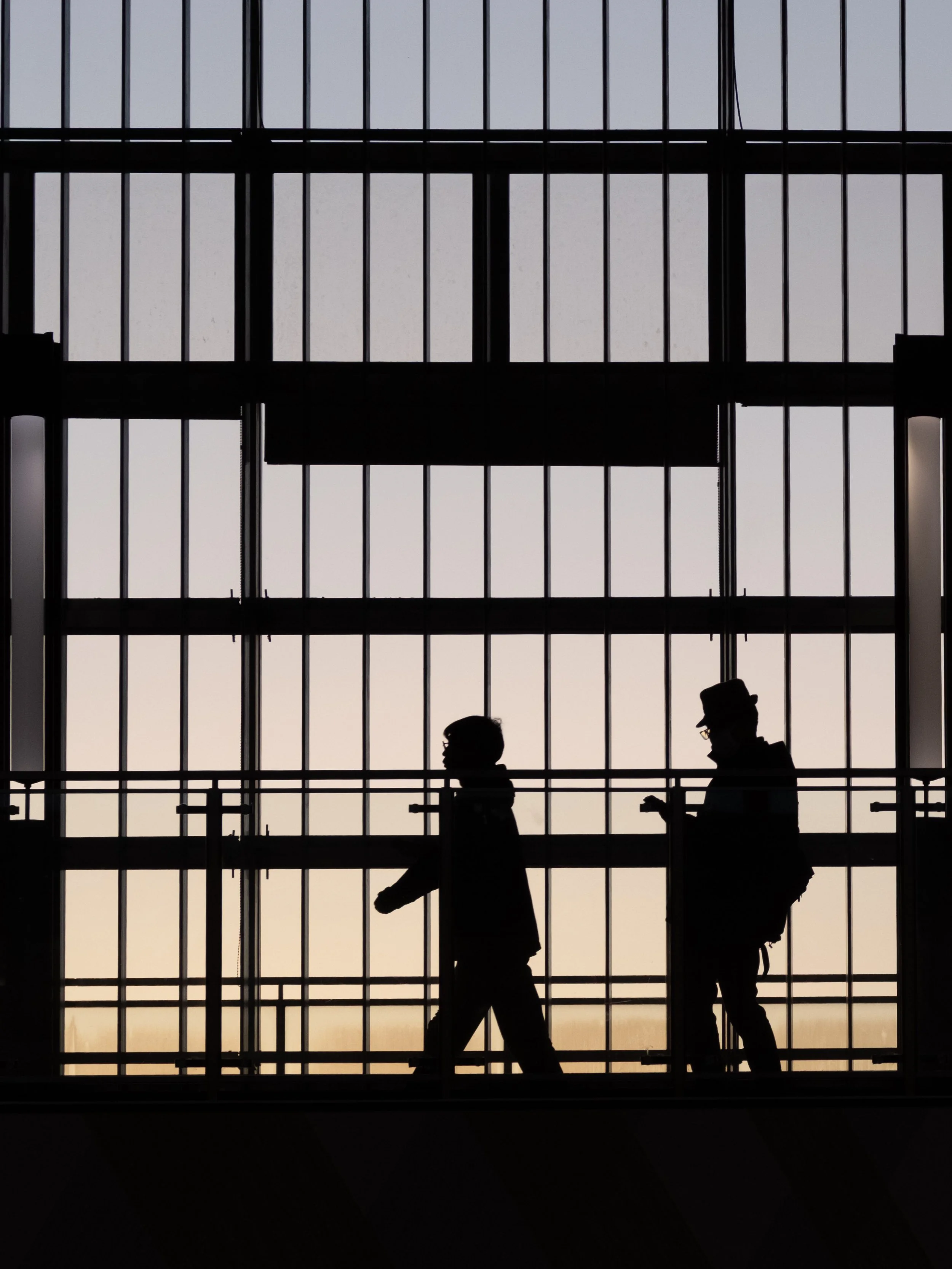 Silhouette von zwei Personen, die auf einer Brücke gehen, gegen den Himmel bei Sonnenuntergang, im Bahnhof in Tokio.
